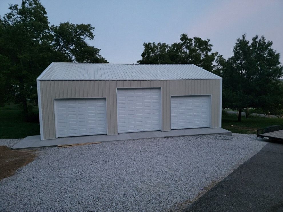 A garage with three garage doors and a trailer parked in front of it.