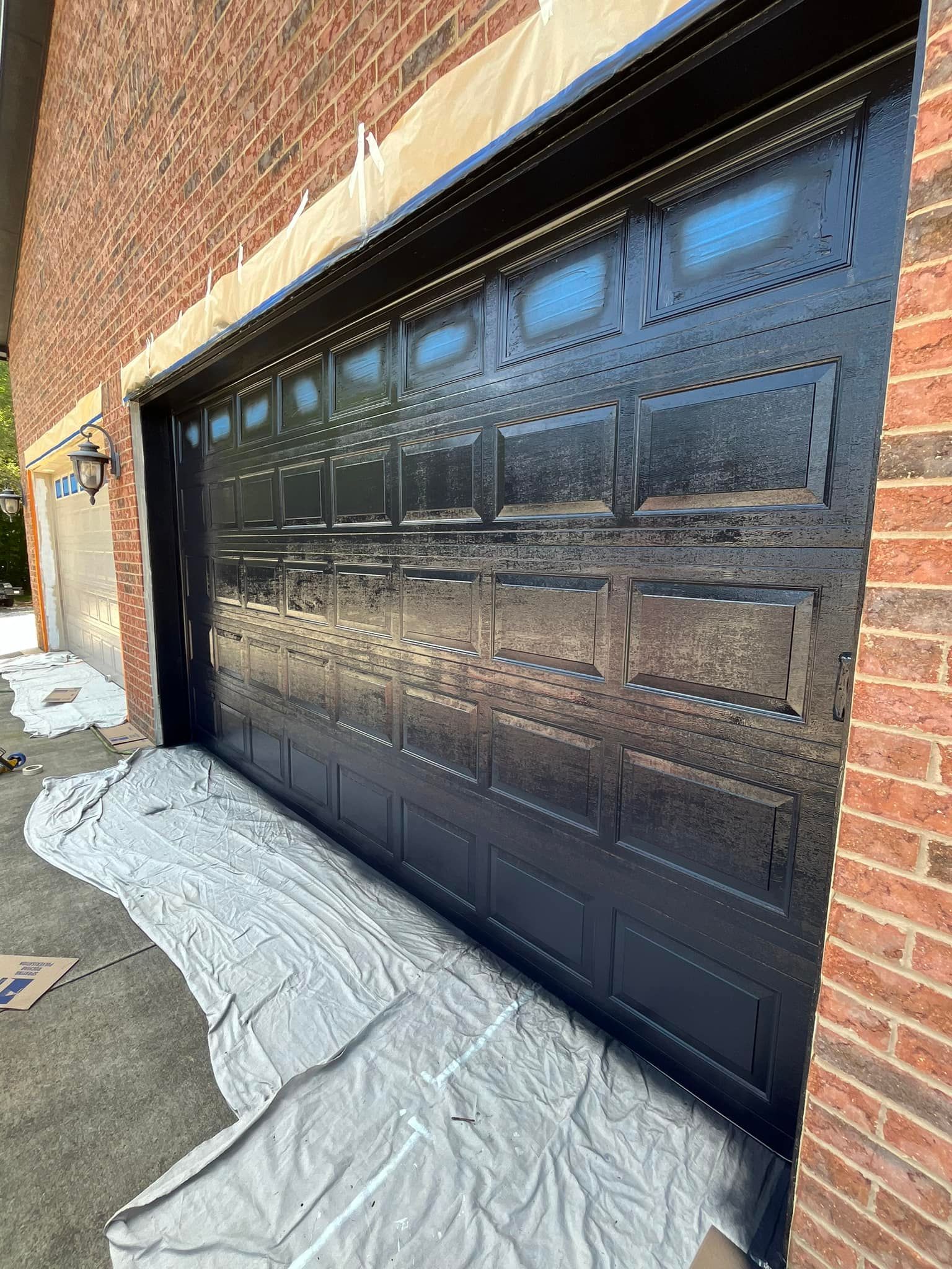 A black garage door is being painted on a brick building.