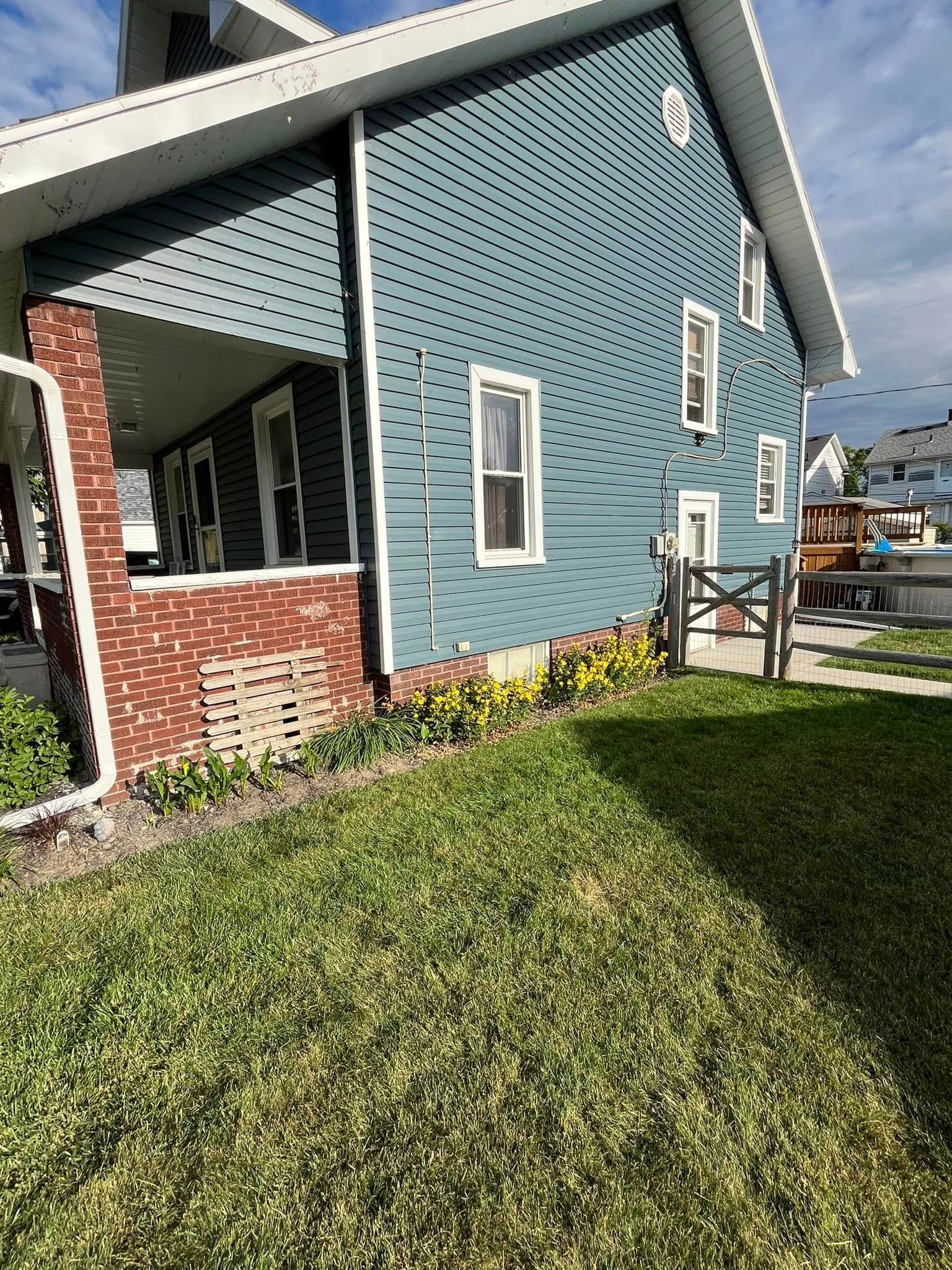 A blue house with a brick porch and a large lawn in front of it.