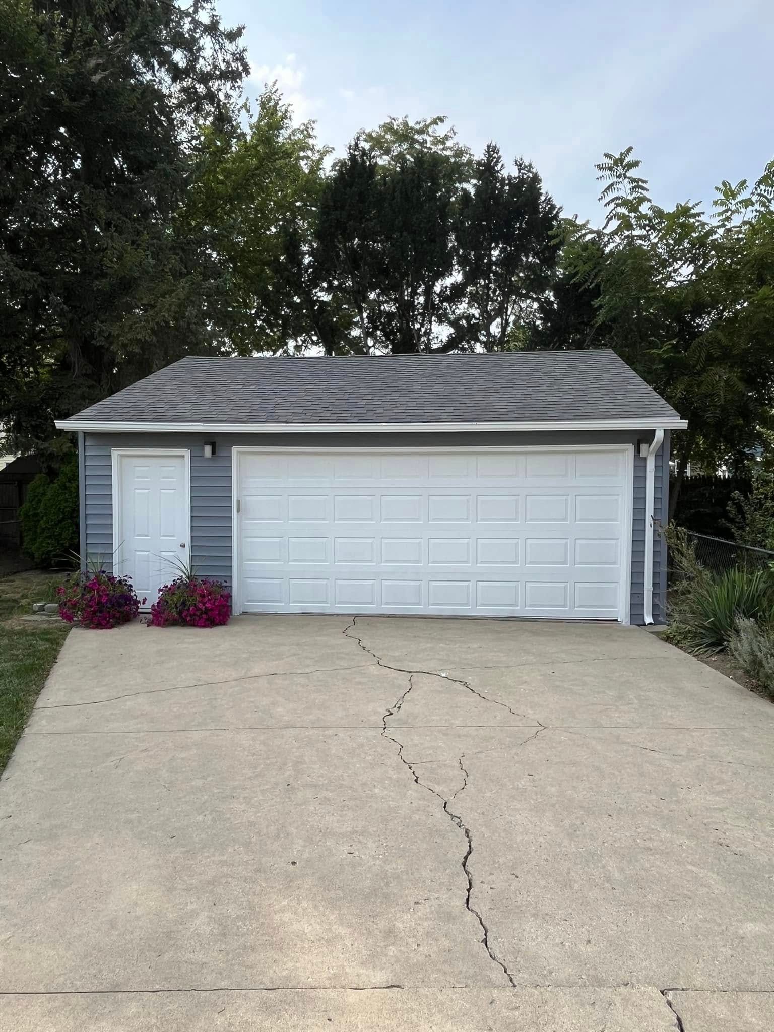 A garage with a gray siding and white garage doors