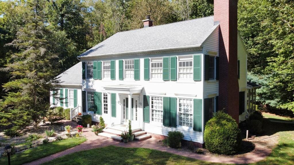 A large white house with green shutters is surrounded by trees.