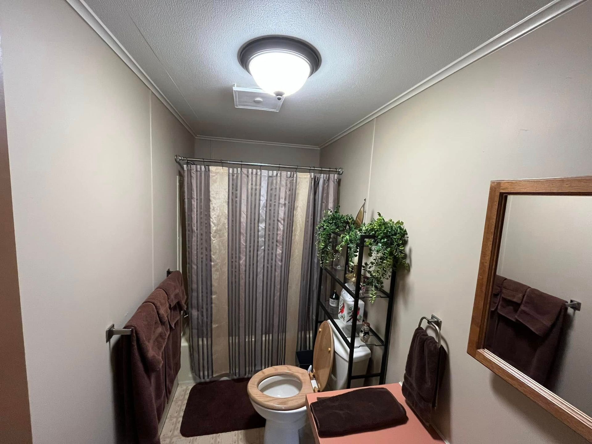 A bathroom with a toilet , sink , mirror and shower curtain.