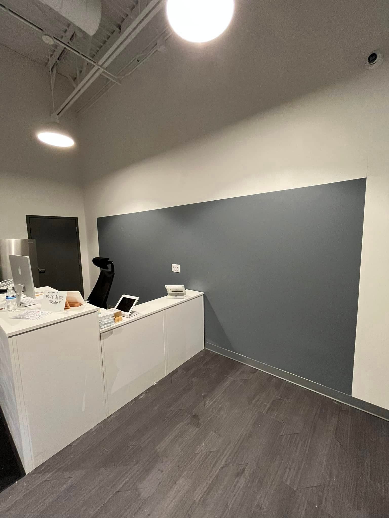 A room with a gray wall and a desk with a computer on it.
