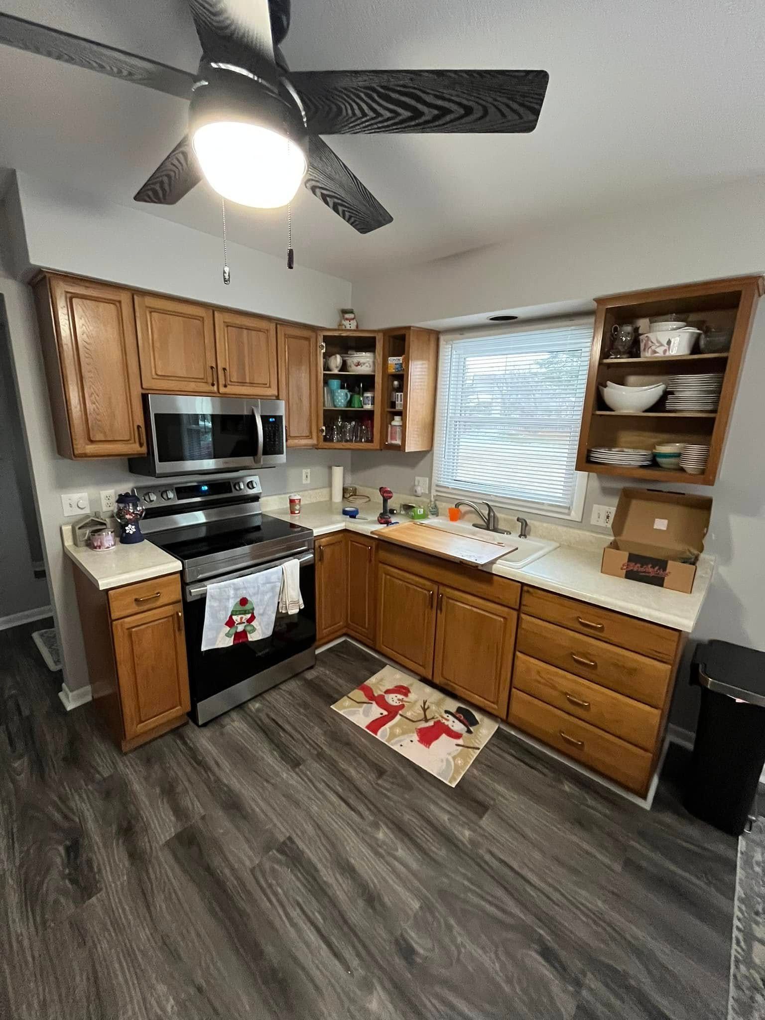 A kitchen with wooden cabinets , stainless steel appliances , and a ceiling fan.