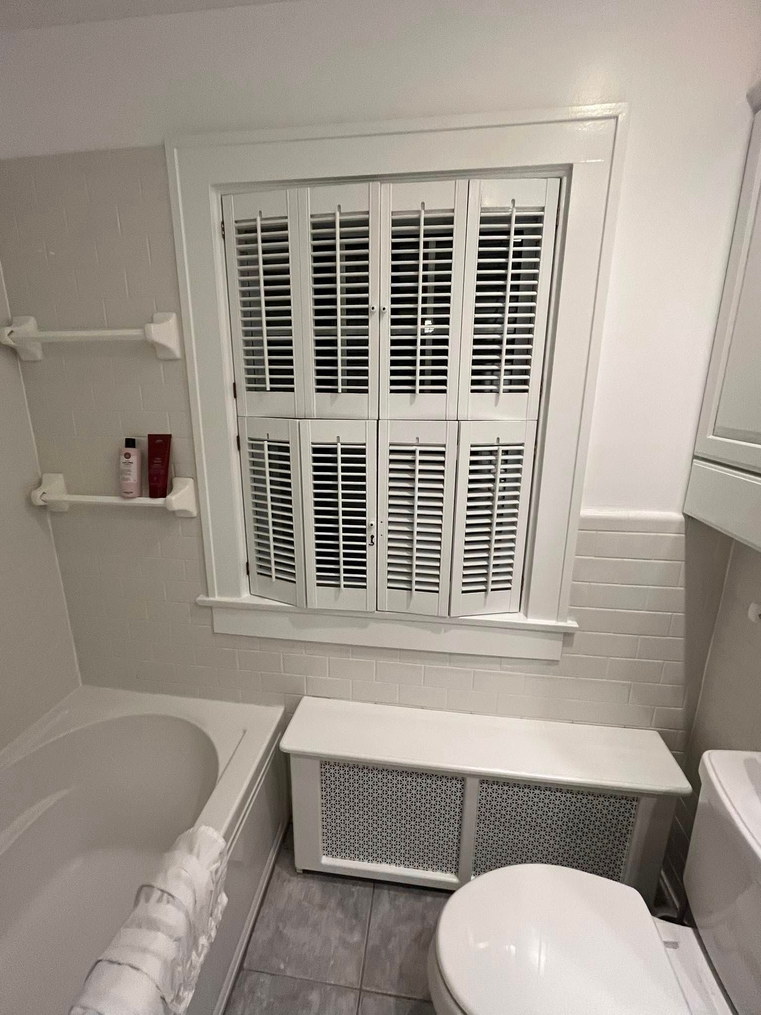 A bathroom with a toilet a bathtub and a window with white shutters
