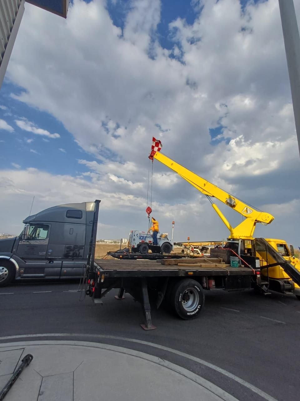 Grúa de plataforma con equipo de elevación amarillo en la cuneta bajo un cielo nublado.
