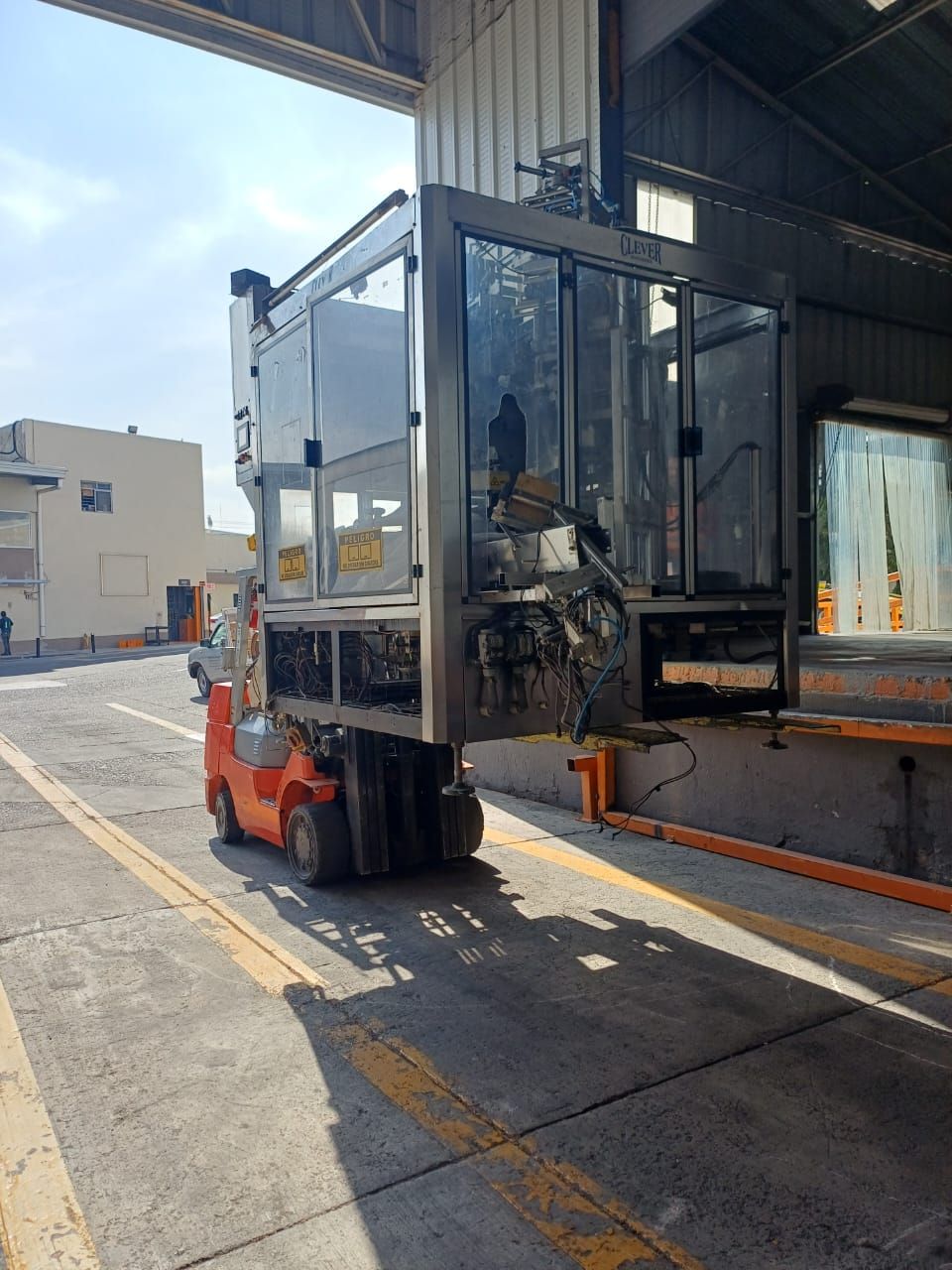 Una carretilla elevadora descarga un contenedor con laterales de cristal en el muelle de un almacén bajo la luz del sol.