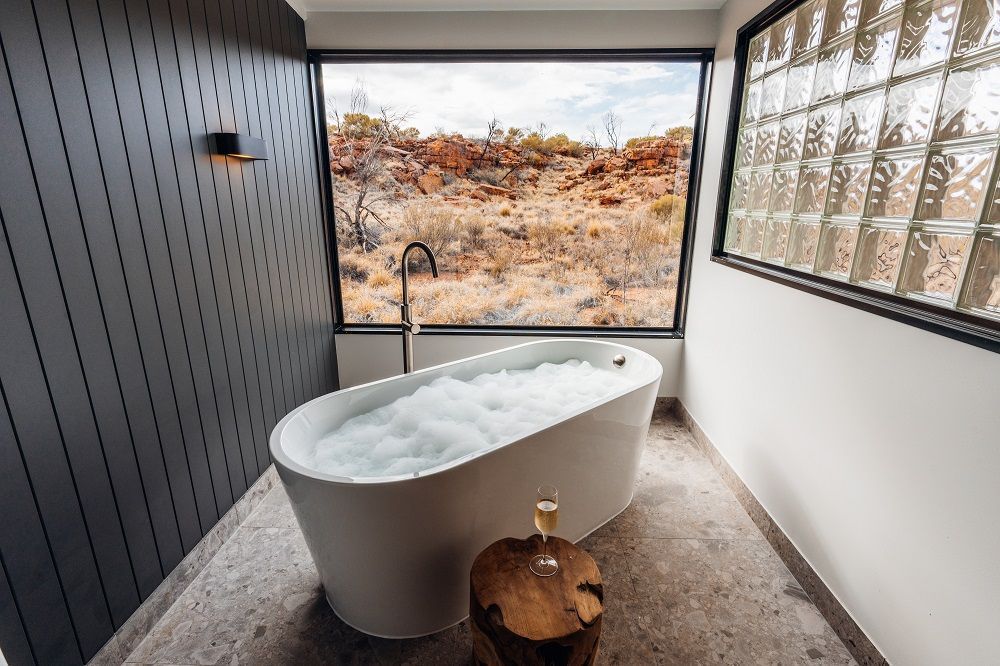 Freestanding bathtub filled with bubbles, facing a large window with desert landscape view.