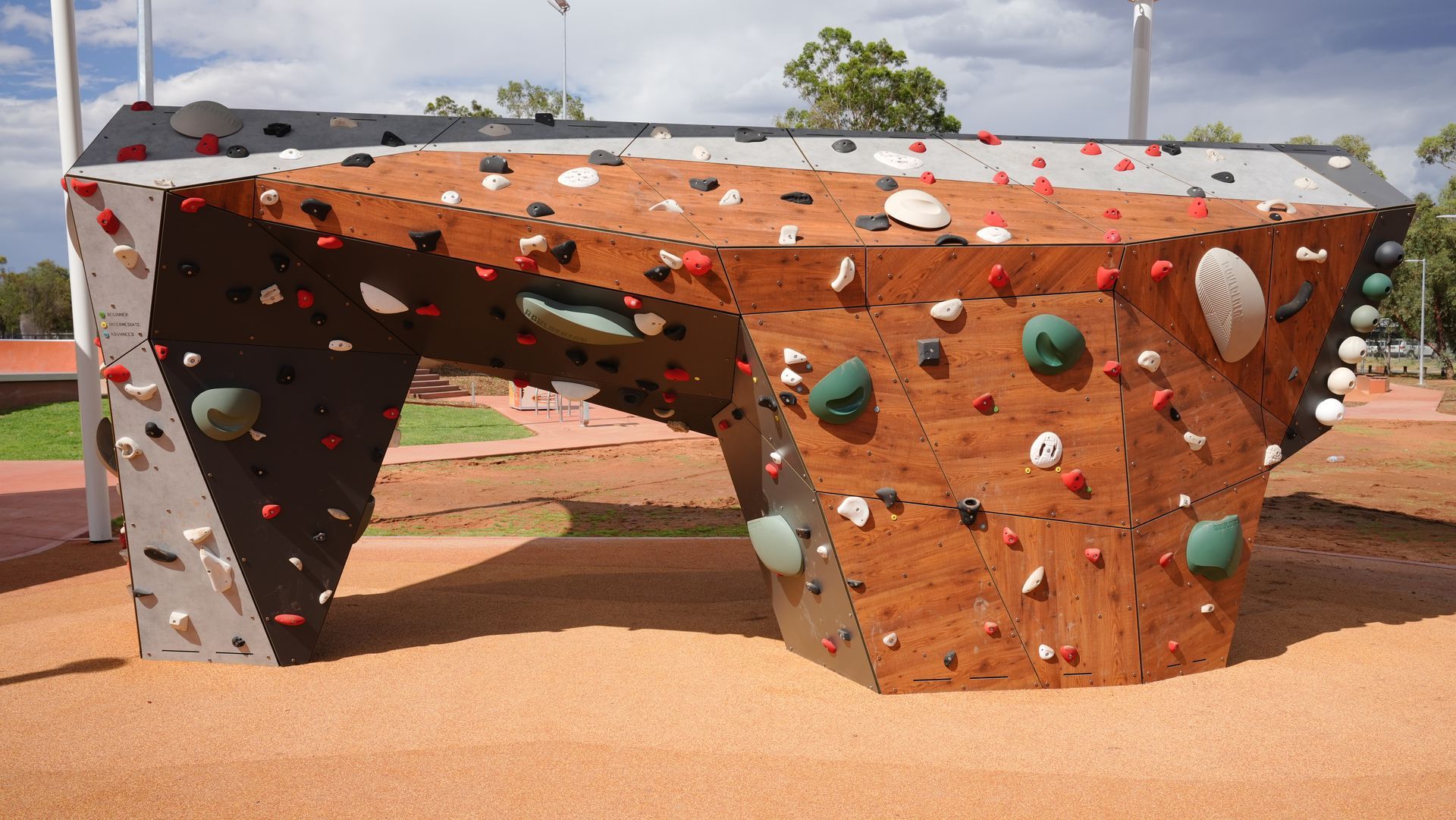 Playground with climbing walls, picnic tables, and shade in a sunny park setting.