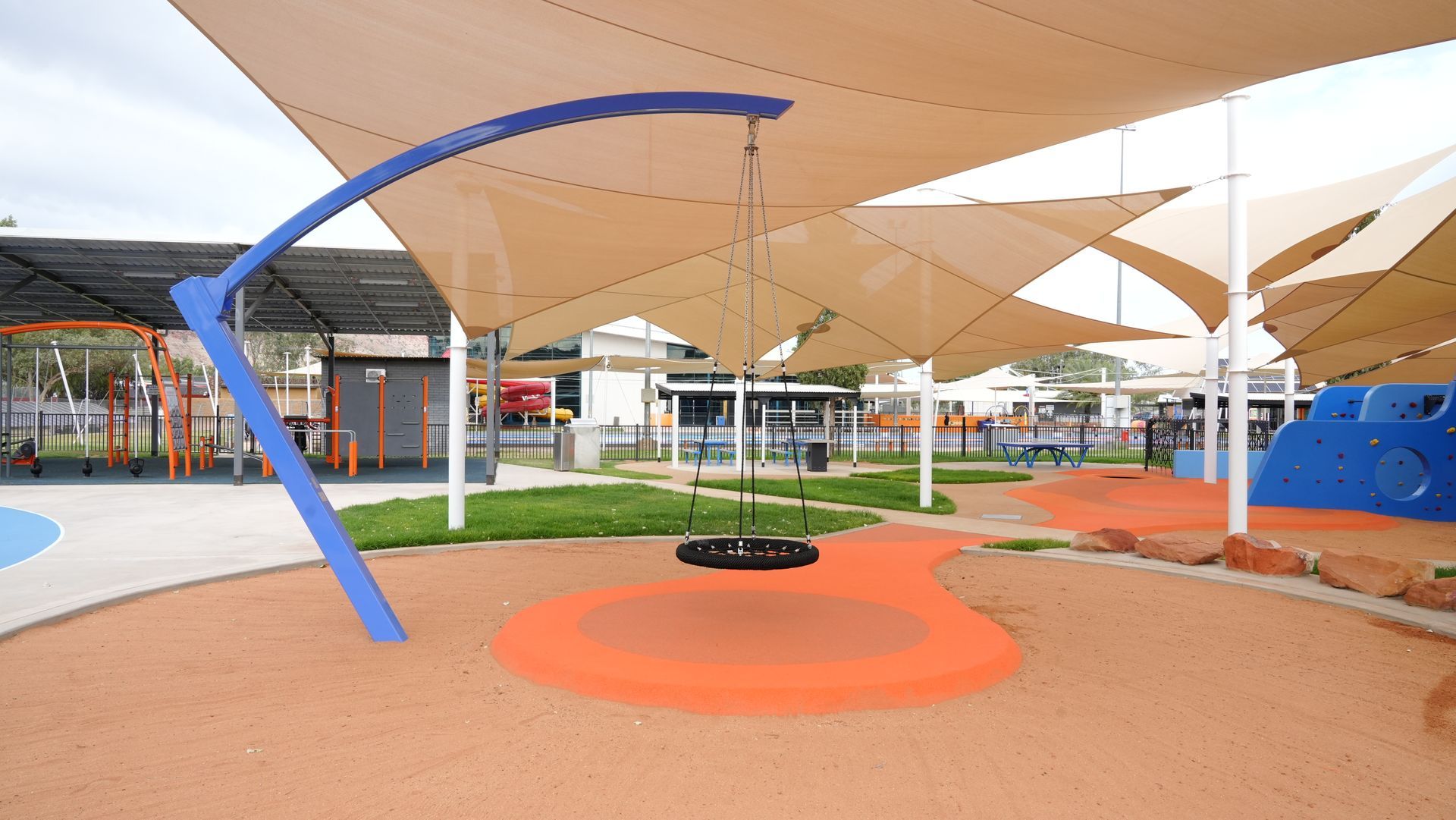 Playground with tire swing, tan shade sails, and orange and blue play areas.