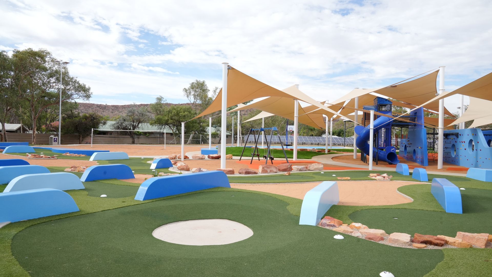 A playground with a slide and umbrellas in a park.