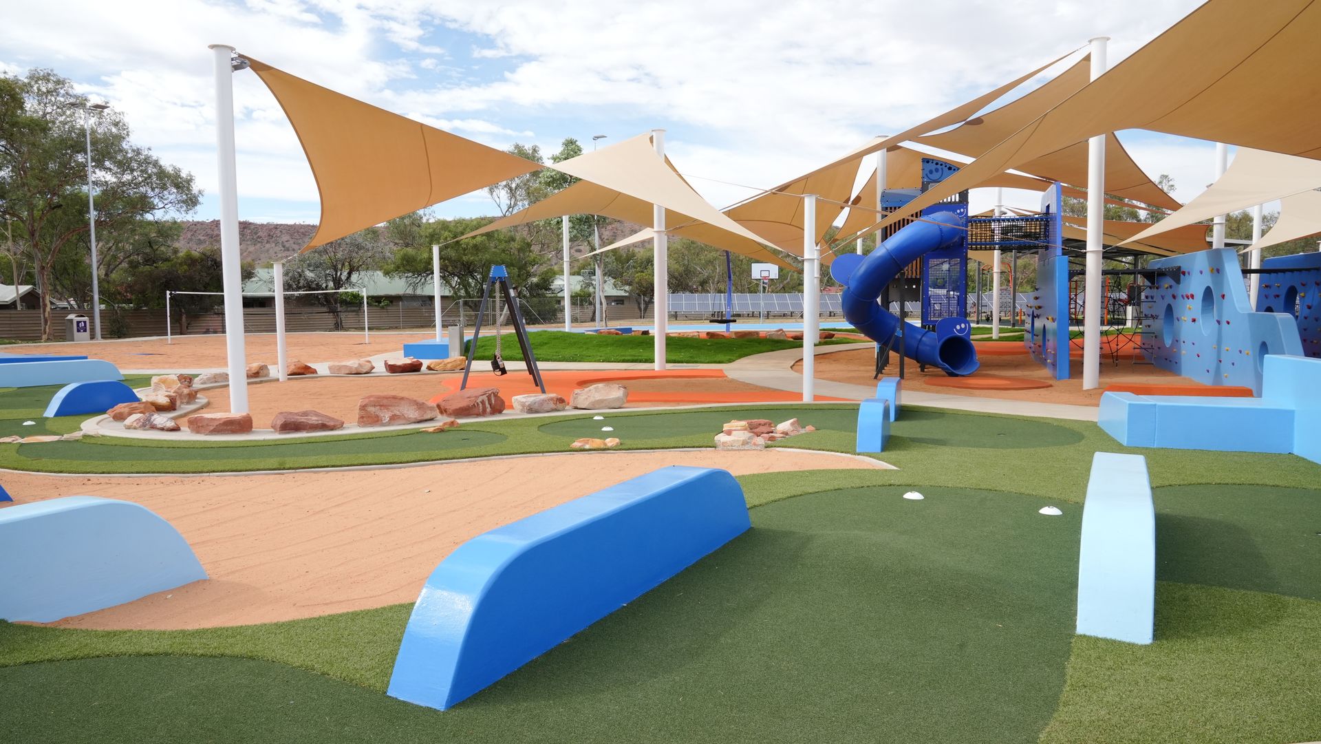 Playground with blue and tan structures, shade sails, and turf.