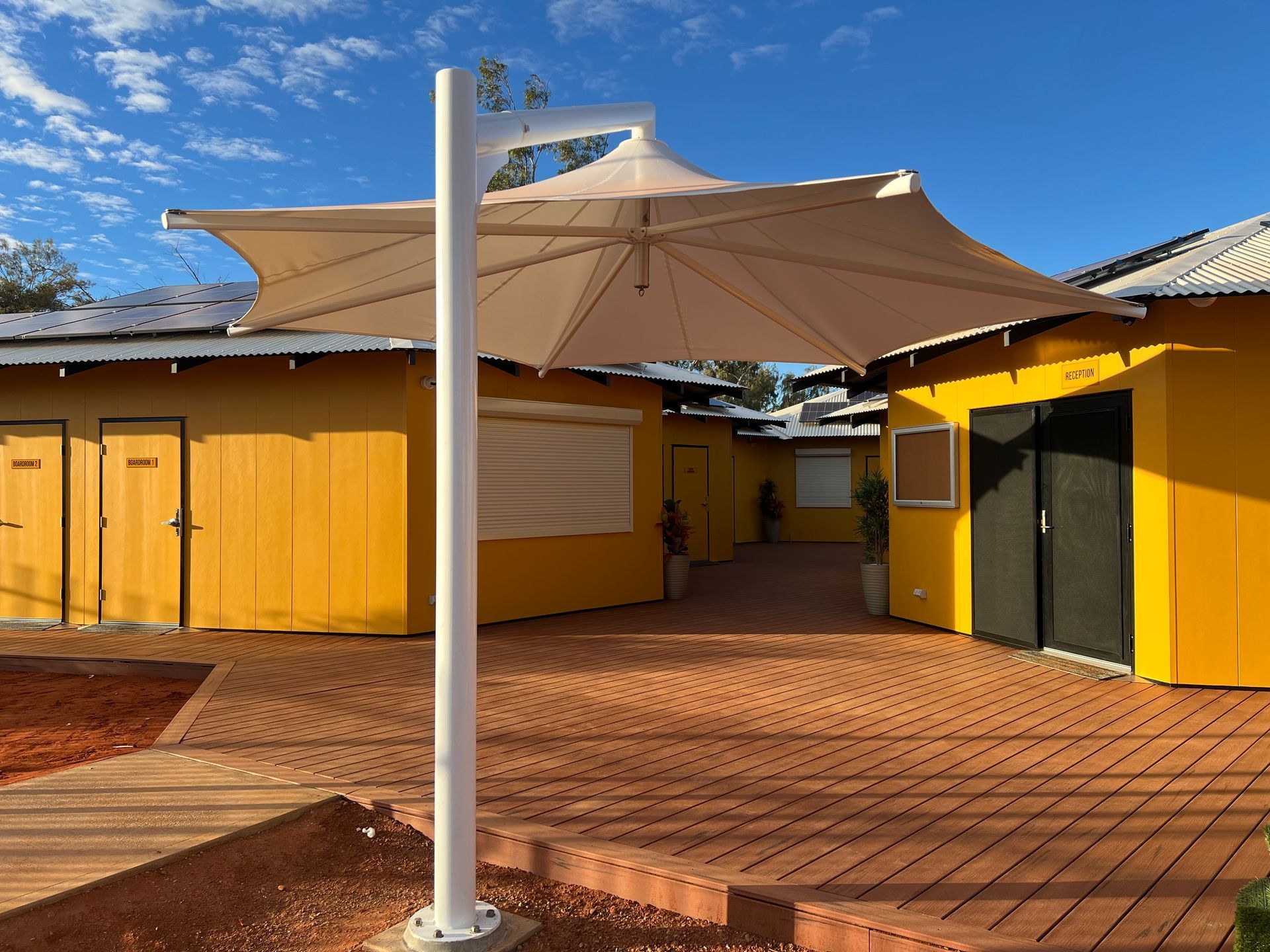 Yellow buildings with brown patio and a beige umbrella on a sunny day.
