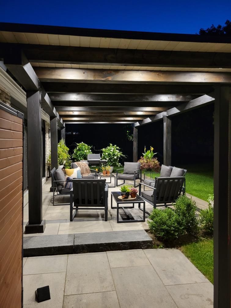 Nighttime patio scene with dark pergola, lit seating area, and plants.