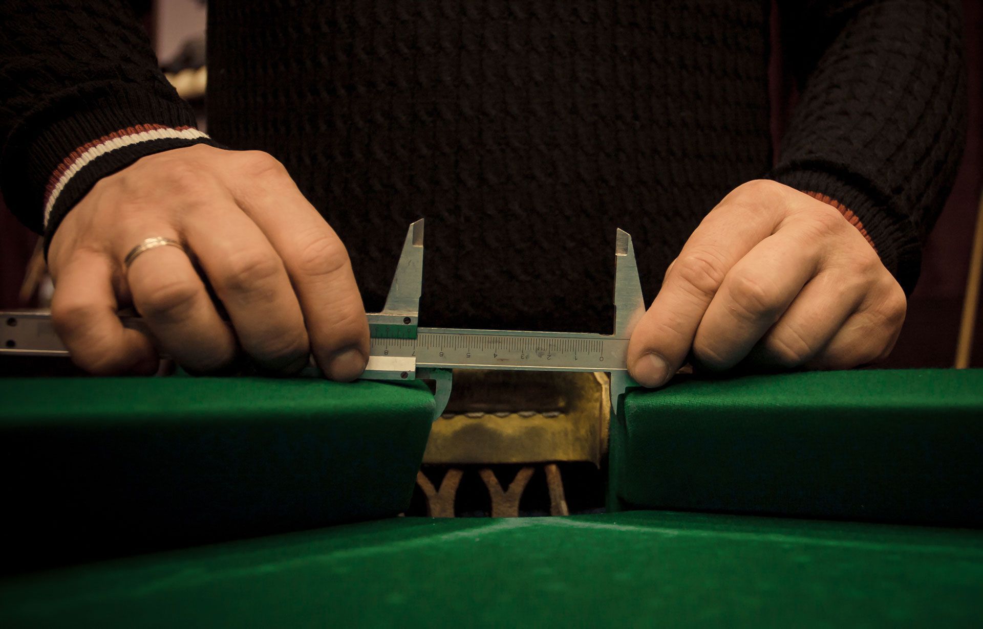 A man is measuring a piece of green cloth with a caliper.