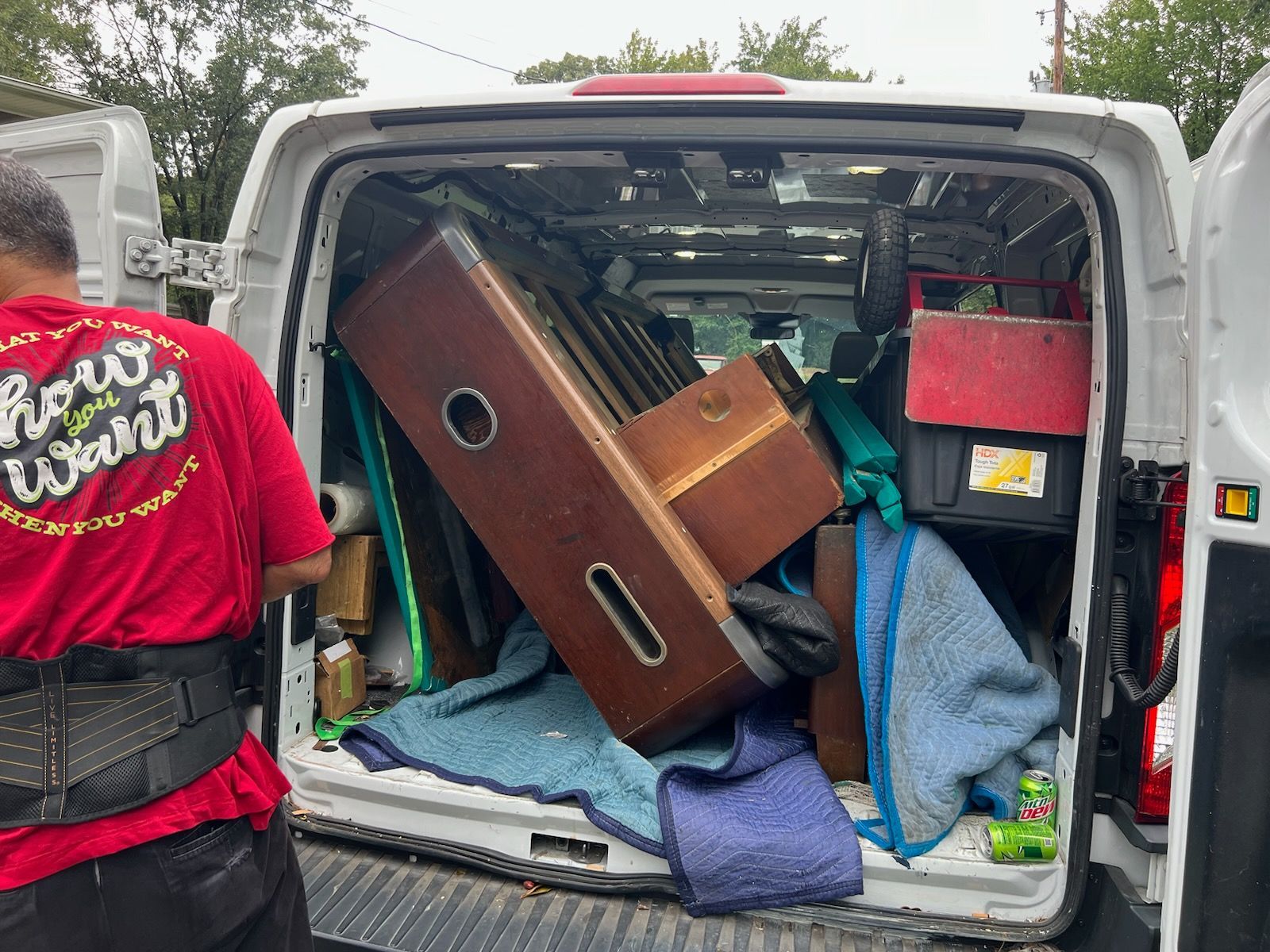 A man in a red shirt is standing in front of a van filled with furniture.