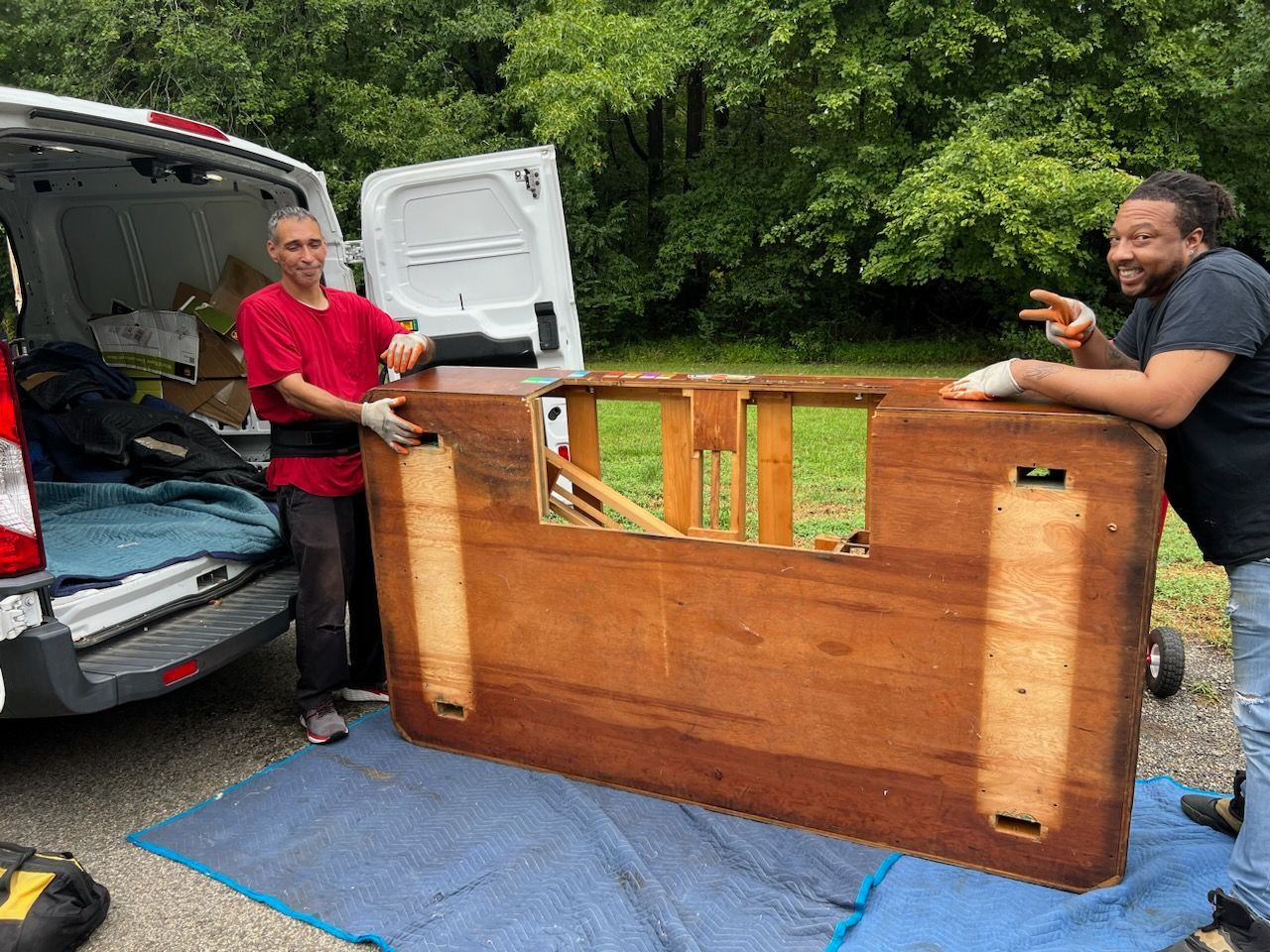 Two men are standing next to a large wooden table in front of a van.