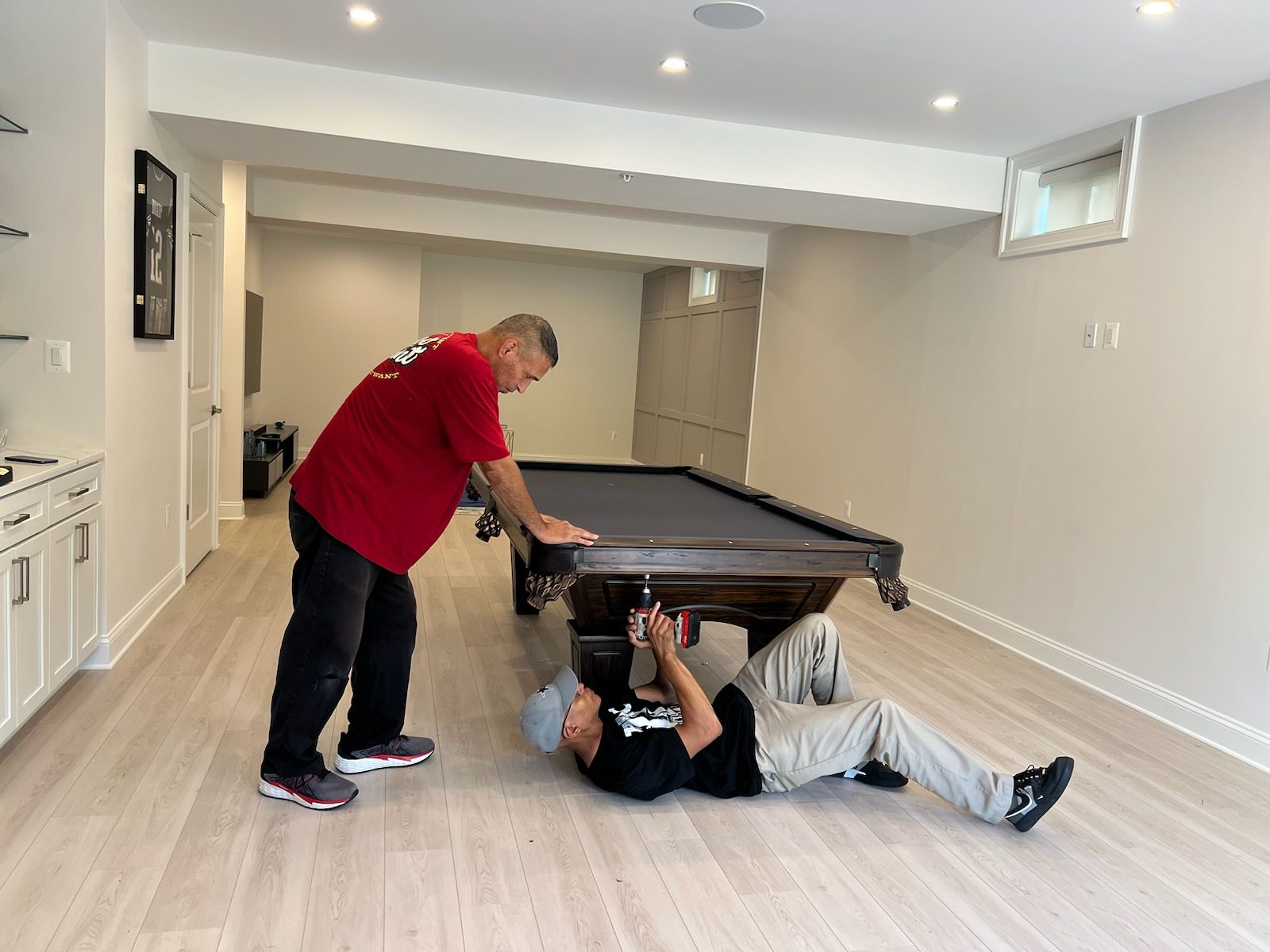 Two men are working on a pool table in a basement.