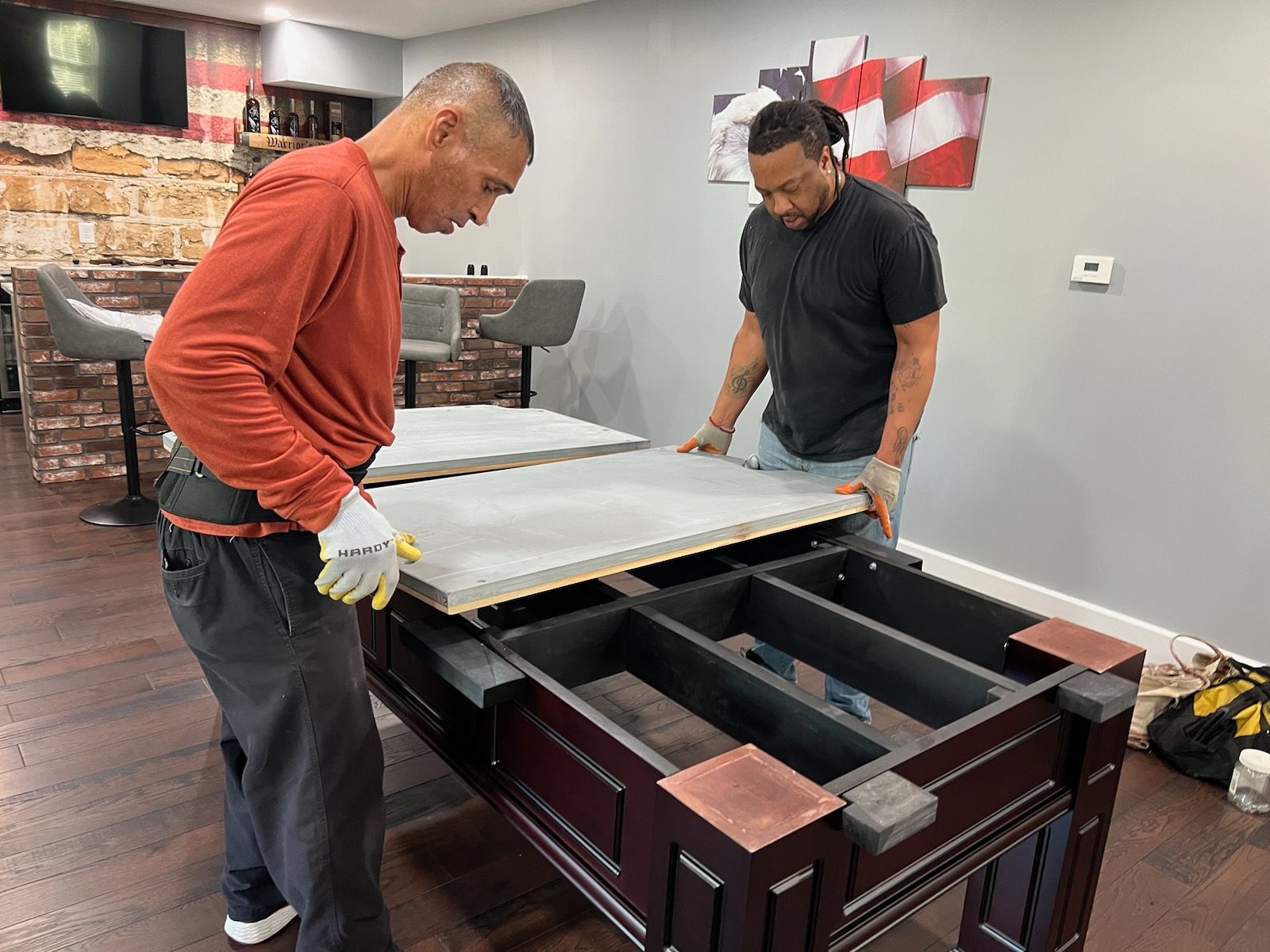 Two men are working on a pool table in a basement.