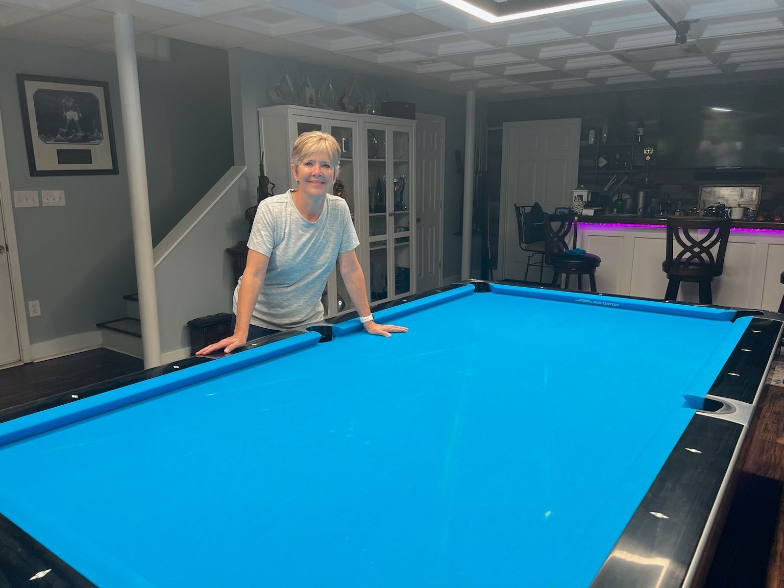 A woman is standing next to a pool table in a basement.
