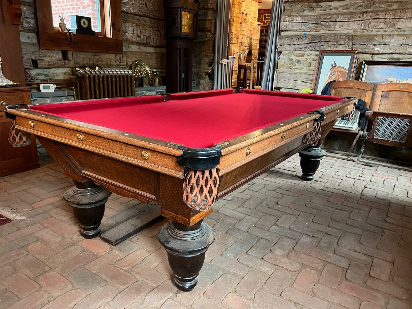 A pool table with a red cloth is sitting on a brick floor in a room.