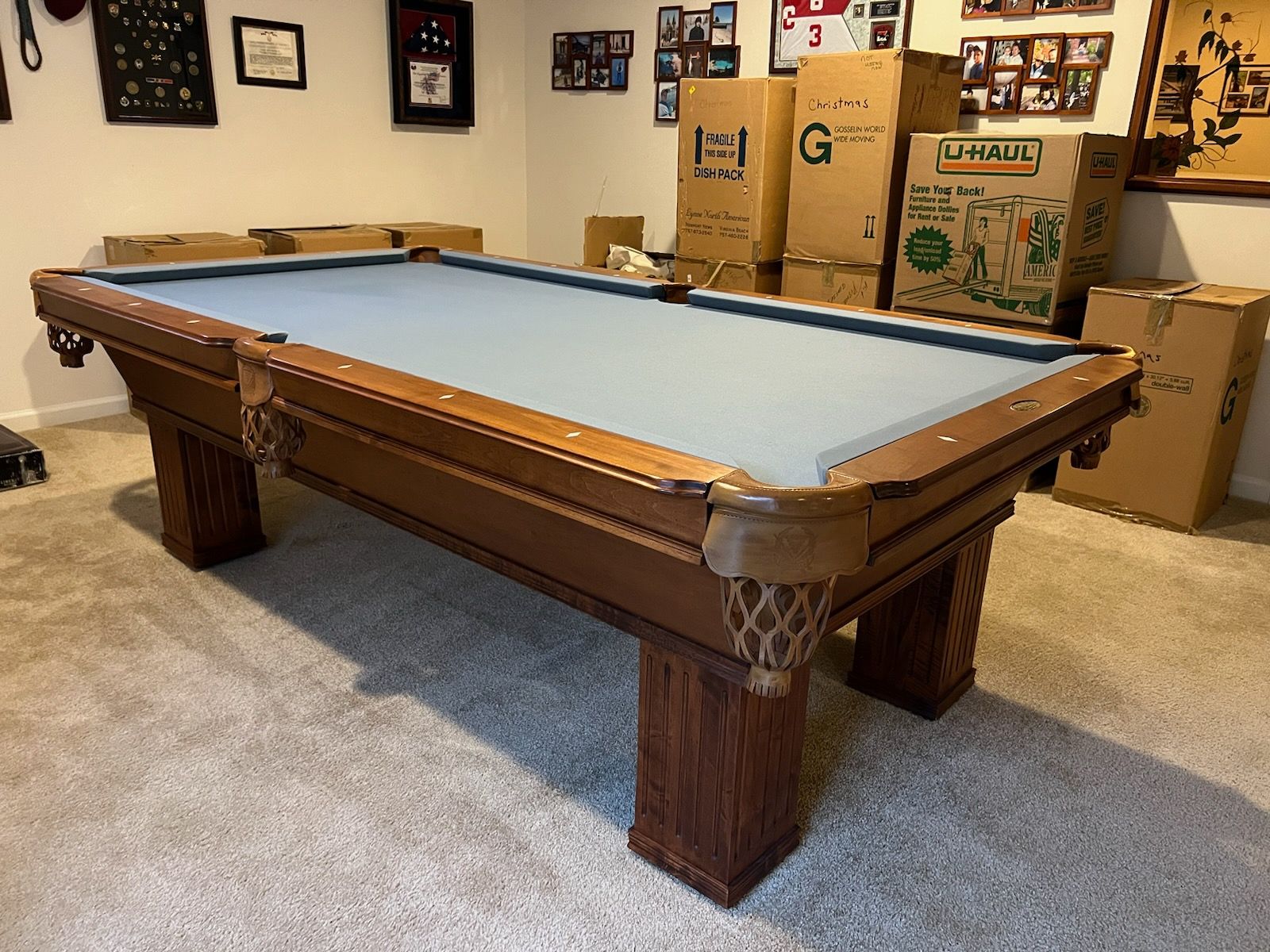 A pool table is sitting in a room surrounded by boxes.
