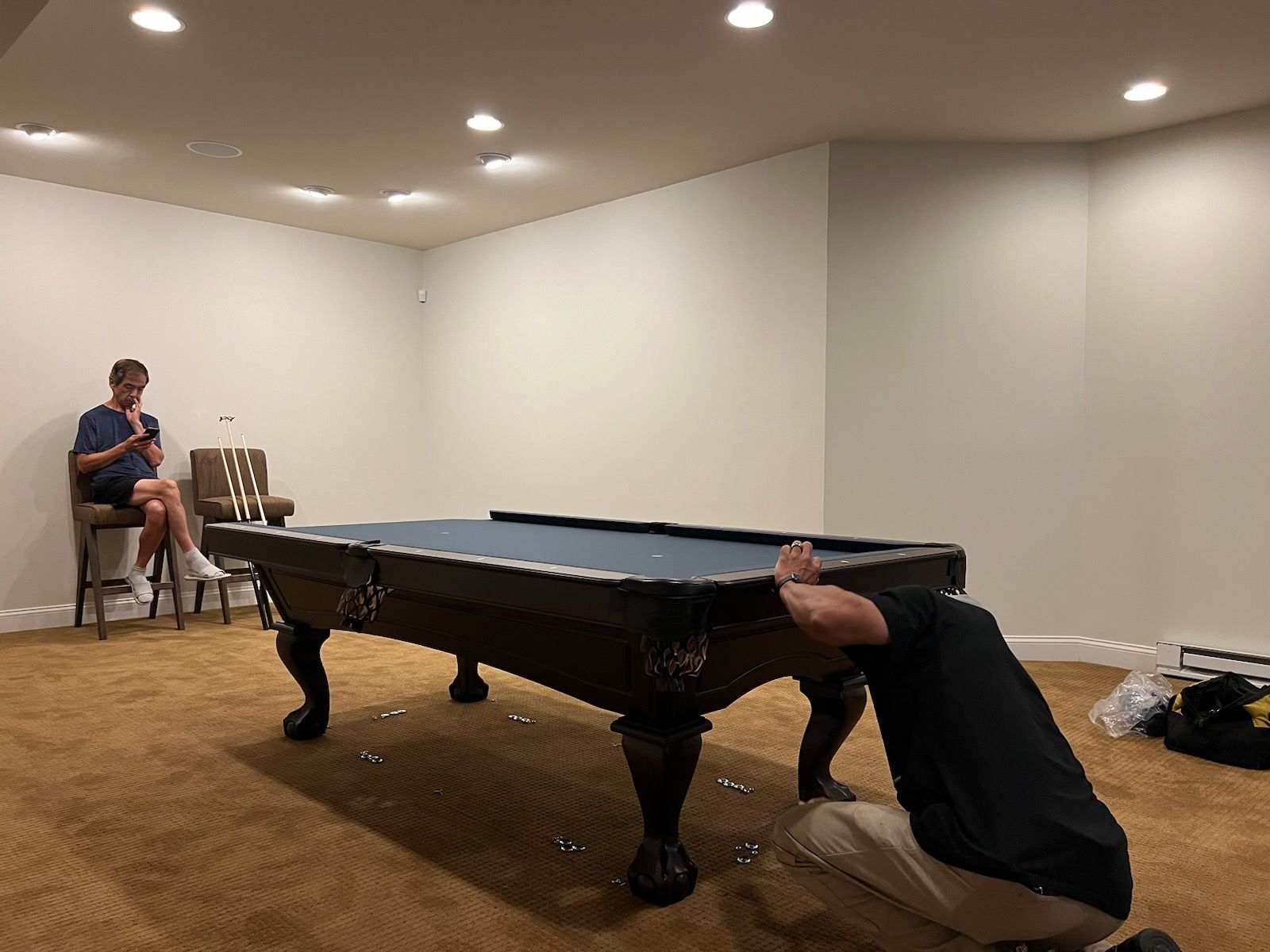 A man is kneeling down in front of a pool table in a basement.
