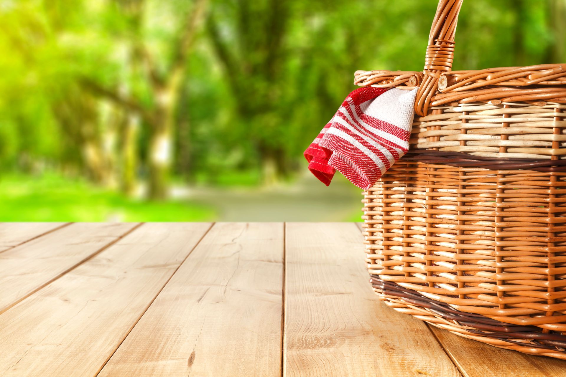 A wicker picnic basket with a red and white towel on a wooden table.