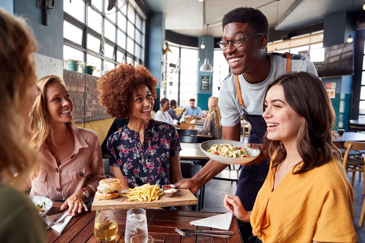 A waiter is serving food to a group of people sitting at a table in a restaurant.