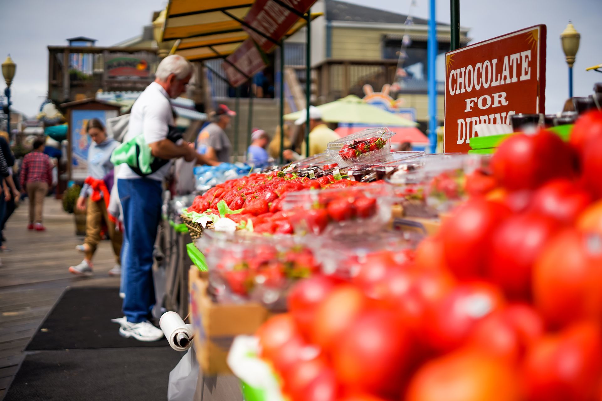 A man is standing in front of a display of strawberries at a market.