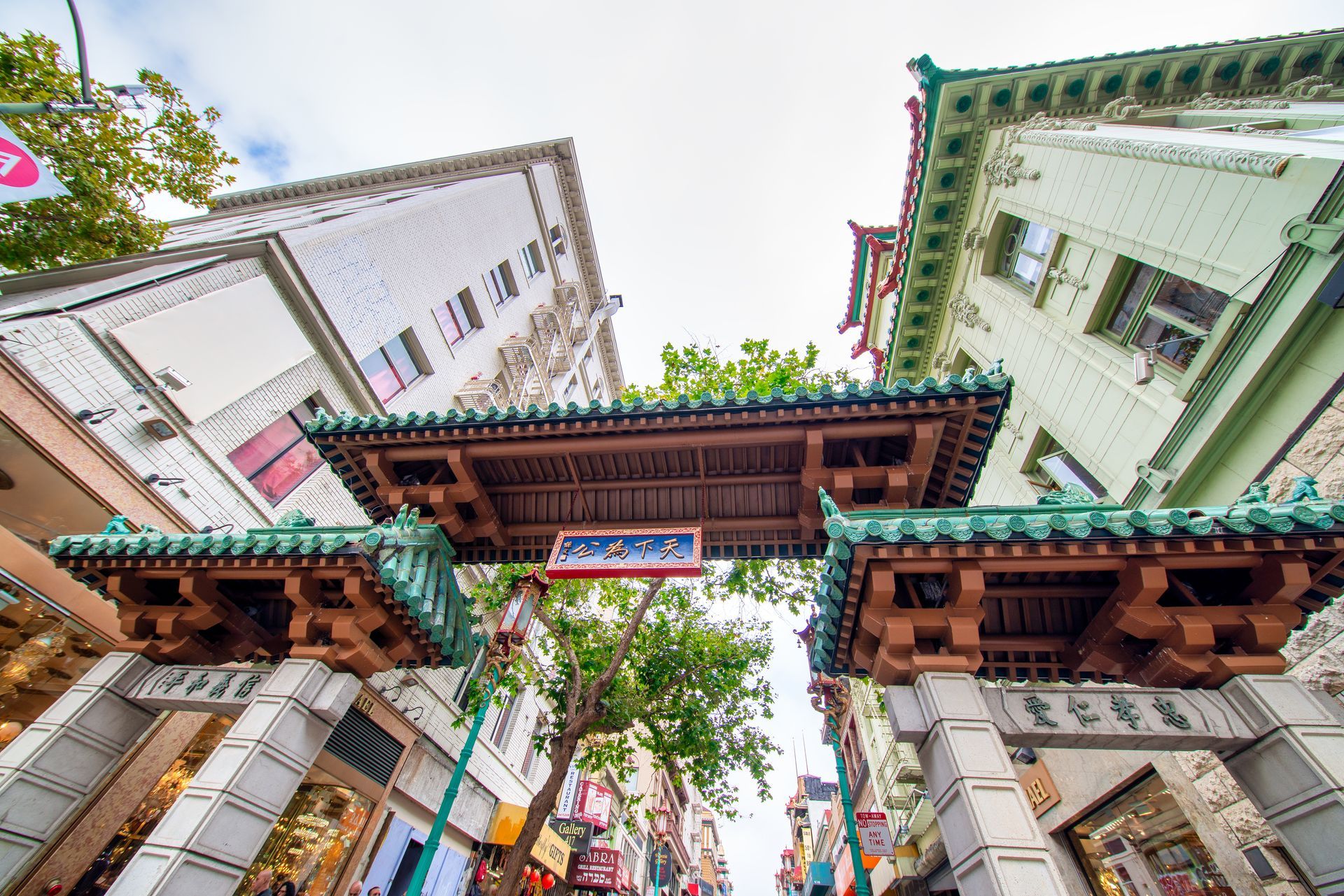Looking up at a chinese archway between two buildings in a city.