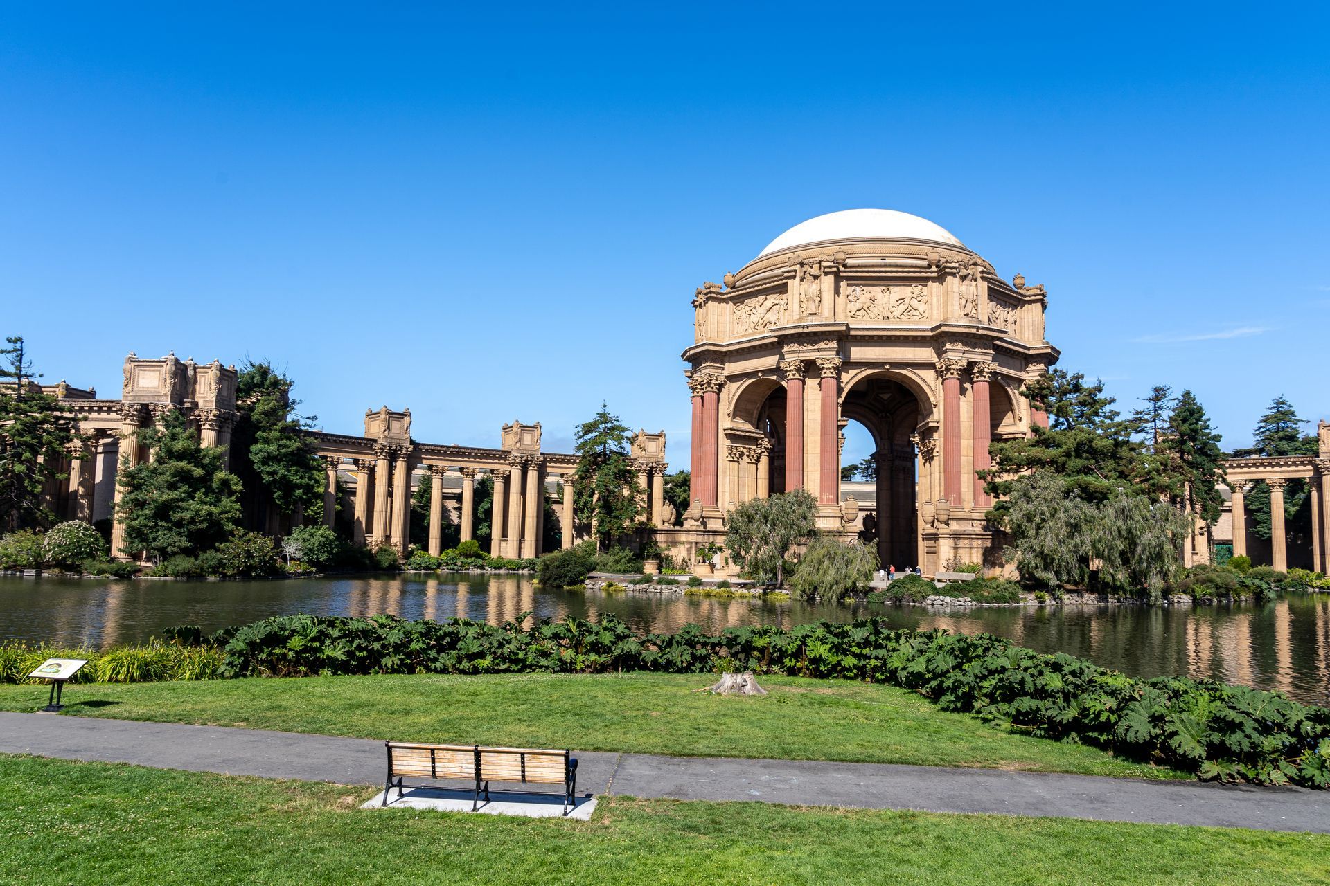 A park with a large building in the background and a bench in the foreground.