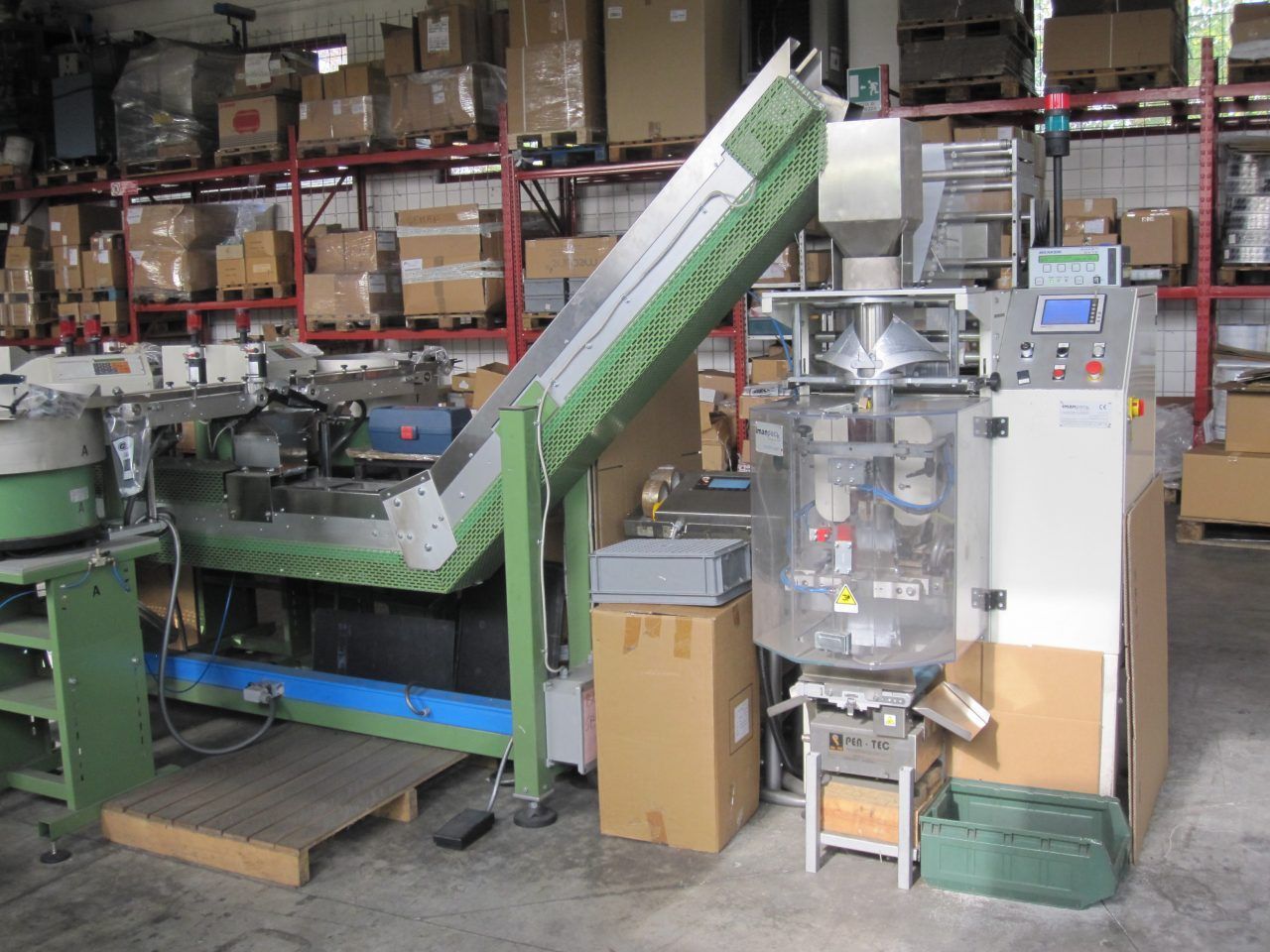 Macchina confezionatrice industriale in magazzino con scatole sugli scaffali.