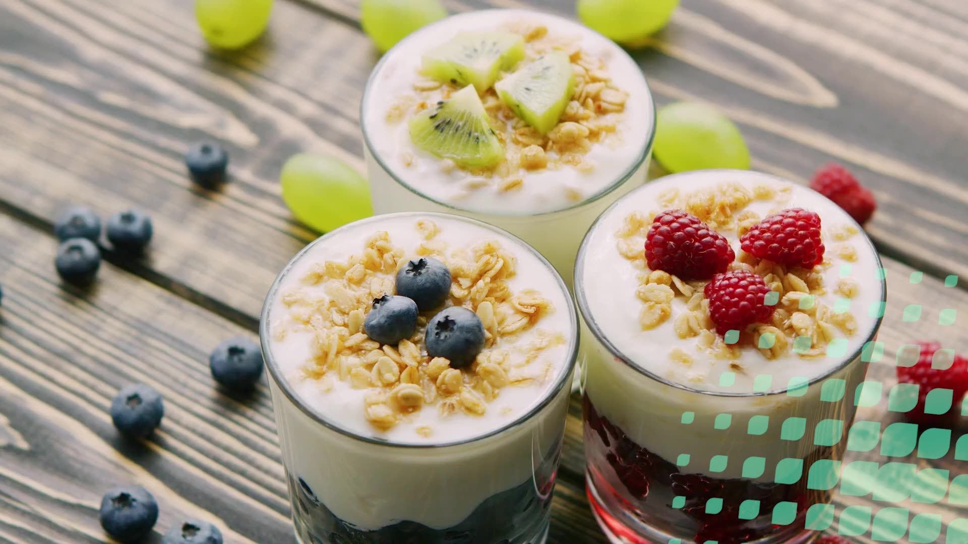Three glasses of yogurt topped with granola and fruit, including blueberries, kiwi, and raspberries, on a wooden surface.
