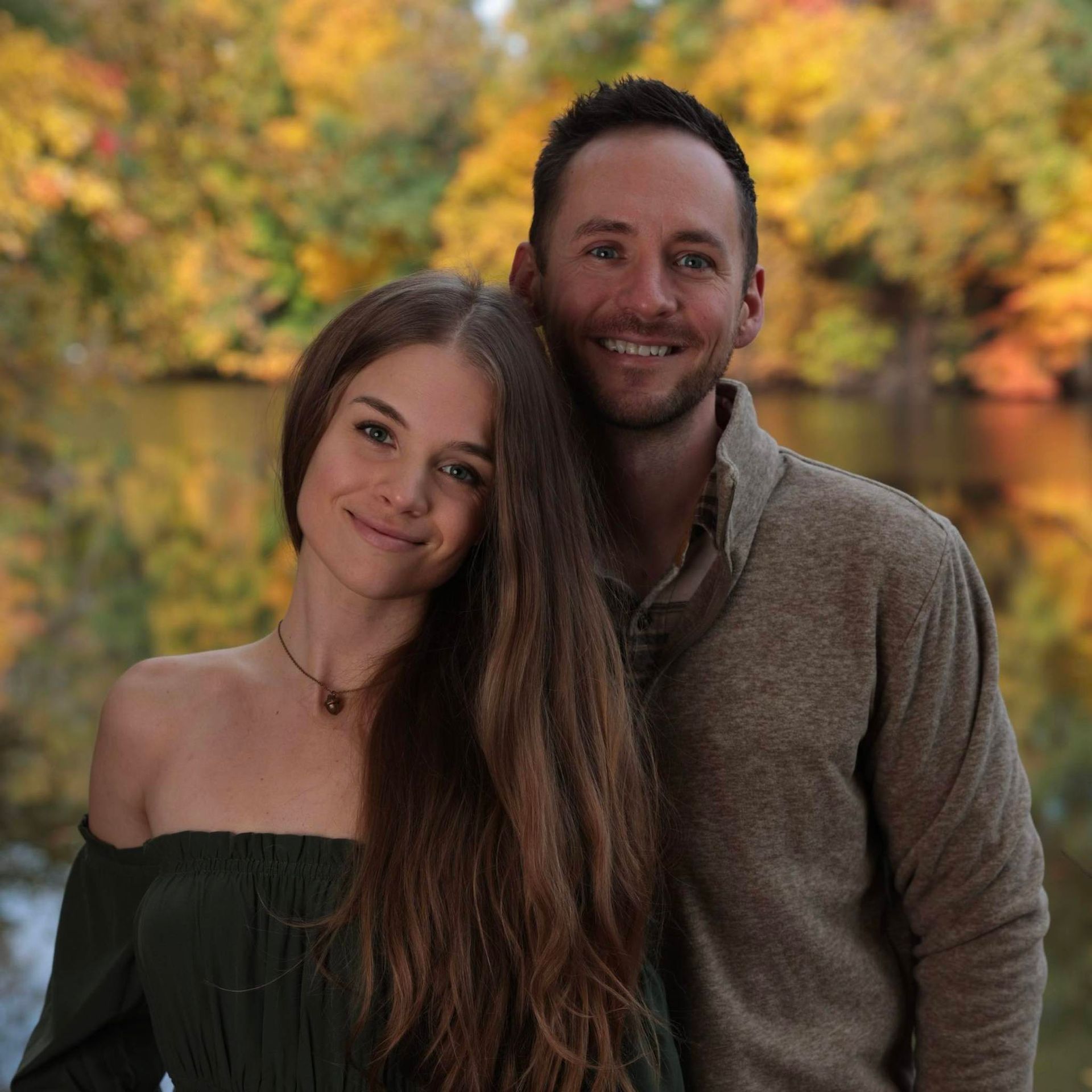 A man and a woman are posing for a picture with trees in the background