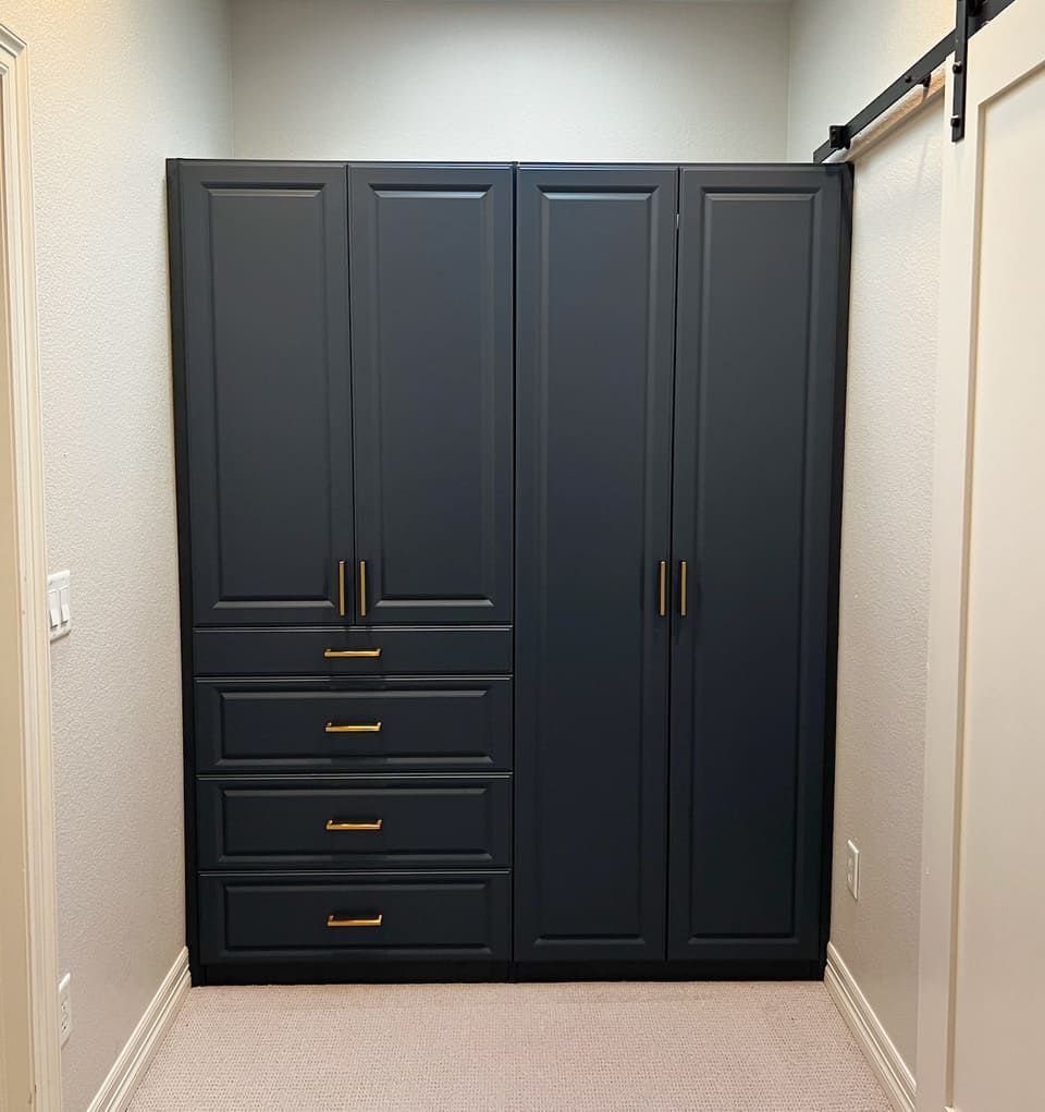 A walk in closet with black cabinets and drawers and a sliding barn door.