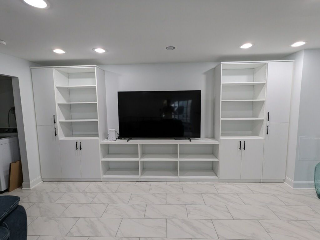 A living room with white cabinets and shelves and a flat screen tv.