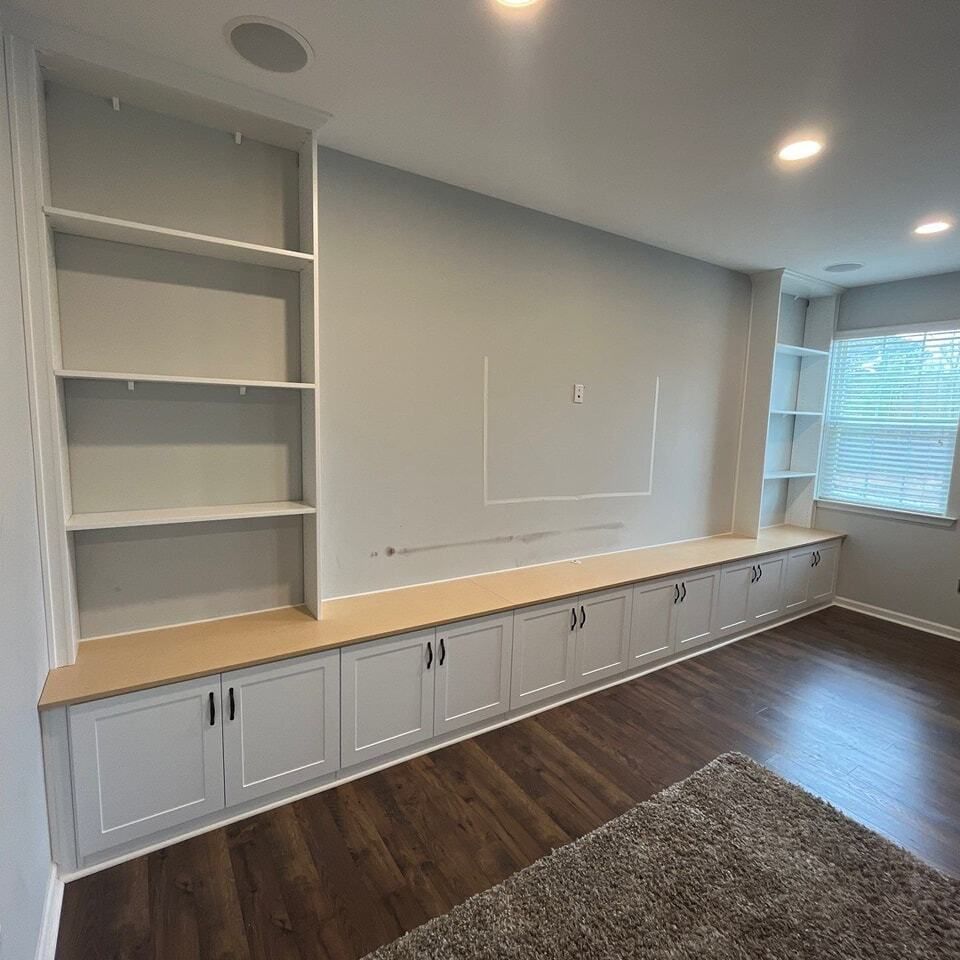A living room with hardwood floors , white cabinets and shelves.