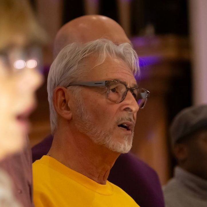 A man with glasses and a beard is wearing a yellow shirt