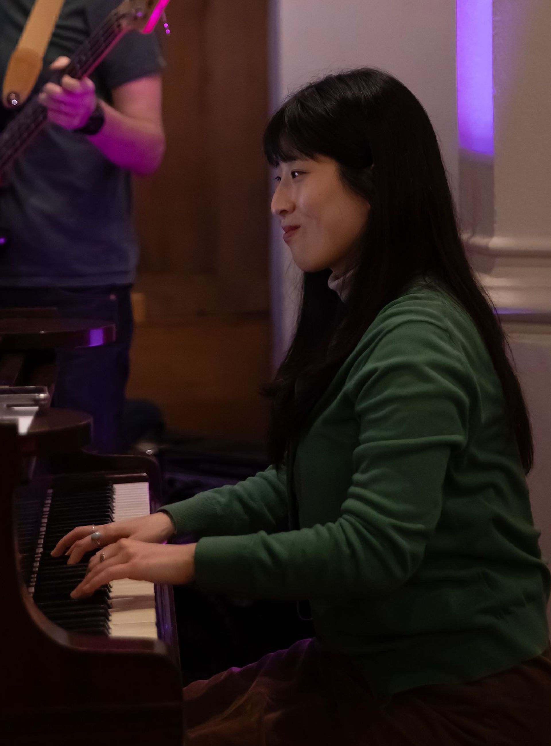 A woman in a green sweater is playing a piano
