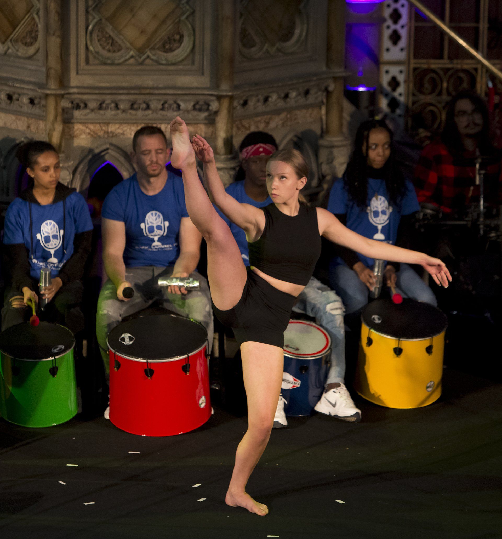 A woman is doing a split in front of a group of drummers