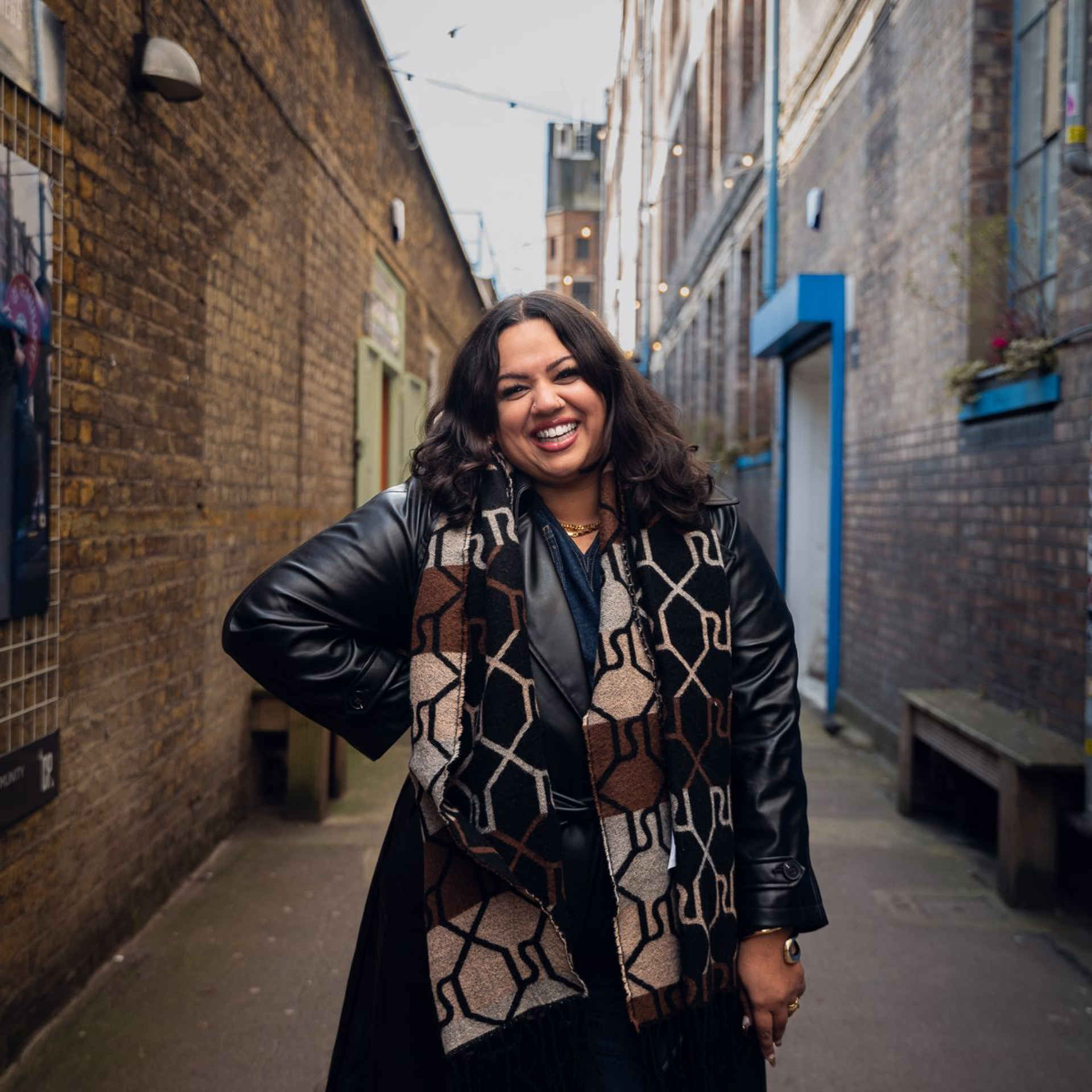 A woman wearing a black leather jacket and geometric patterned scarf is smiling for the camera