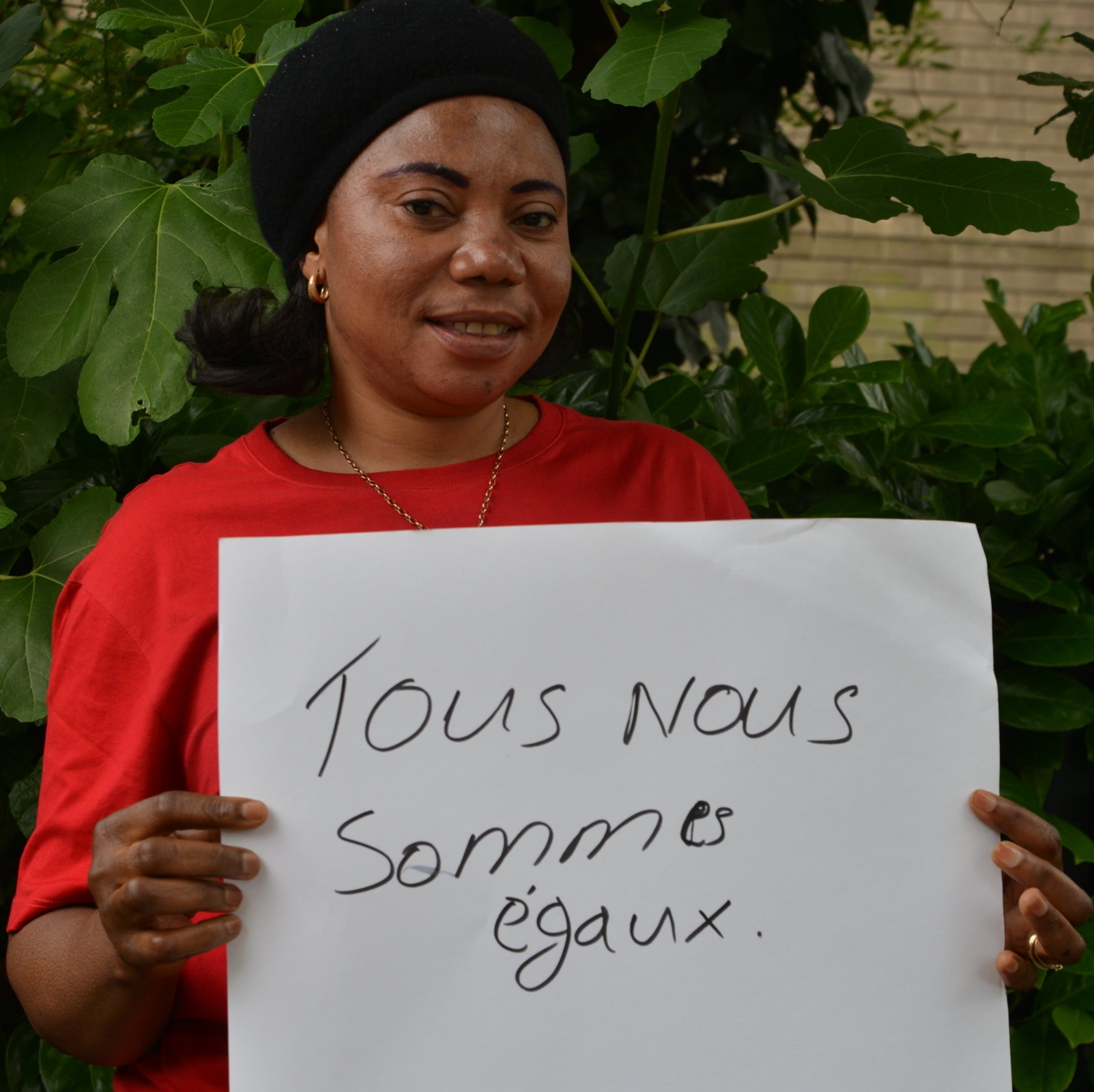 A woman in a red shirt is holding a sign that says tous nous sommes egalx