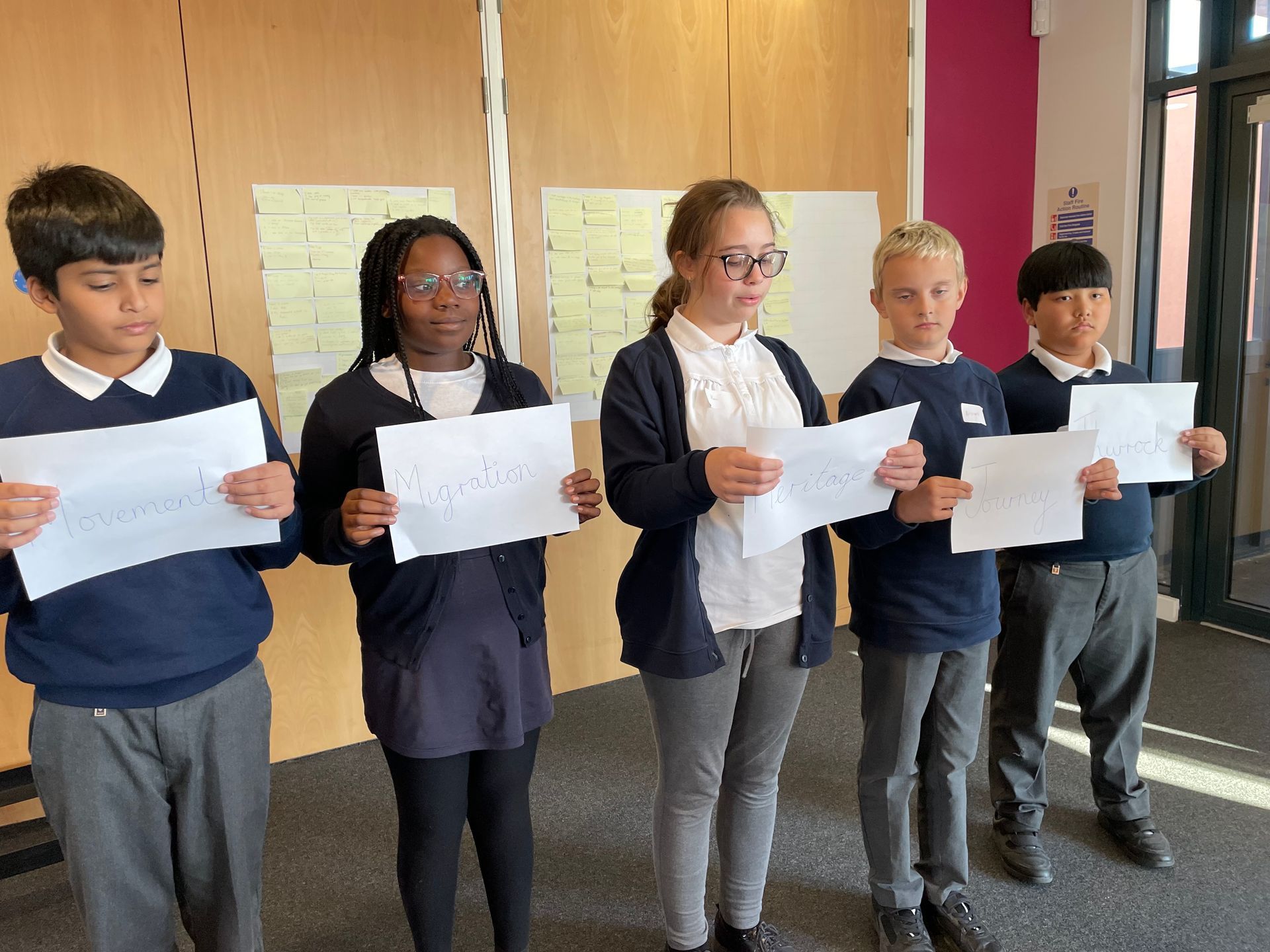 A group of children are standing in a line holding papers.