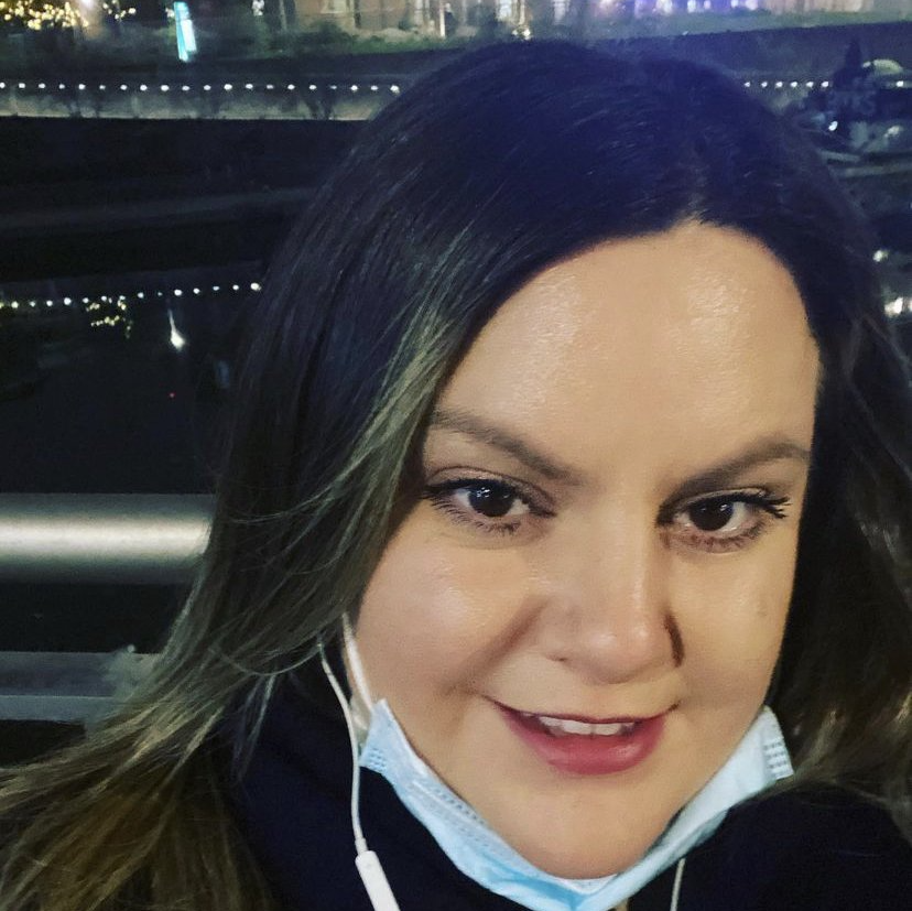 A woman wearing a mask and headphones smiles for the camera