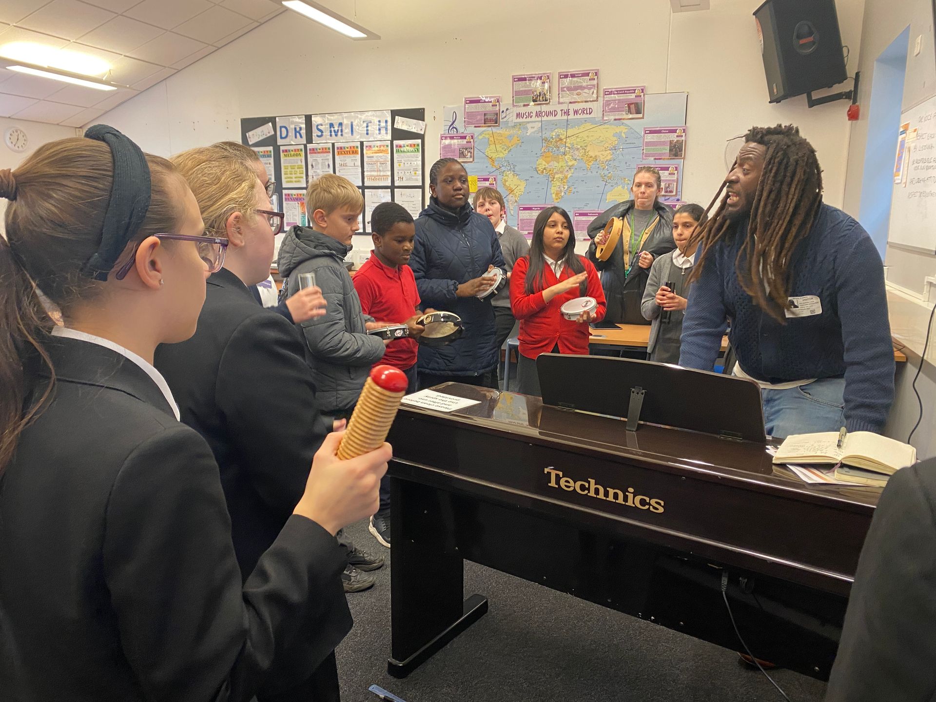 A group of people are standing around a technics piano.