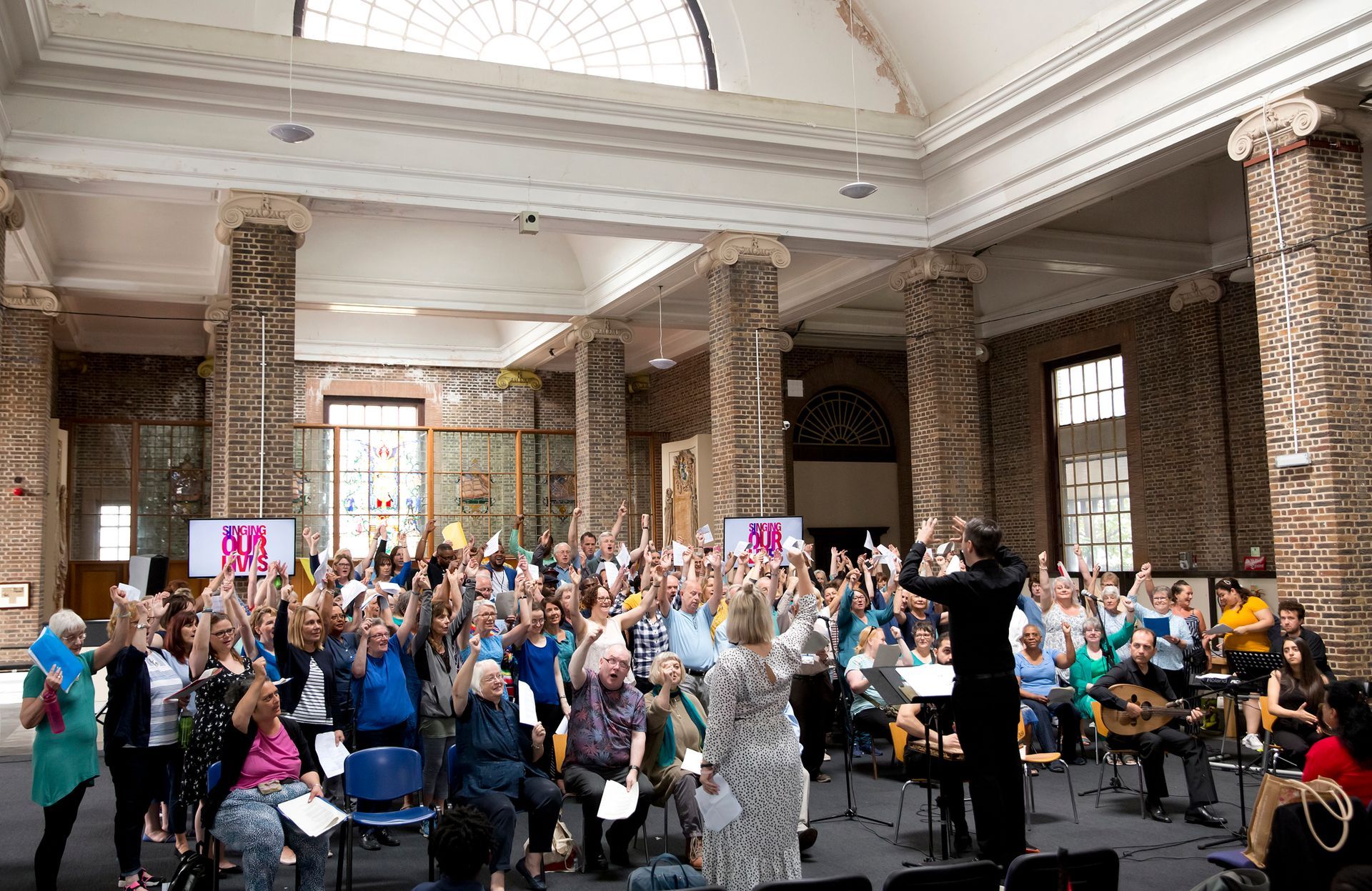 A large group of people are standing in a room with their hands in the air.