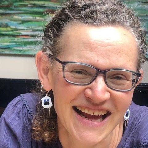 A woman wearing glasses and earrings is smiling for the camera.