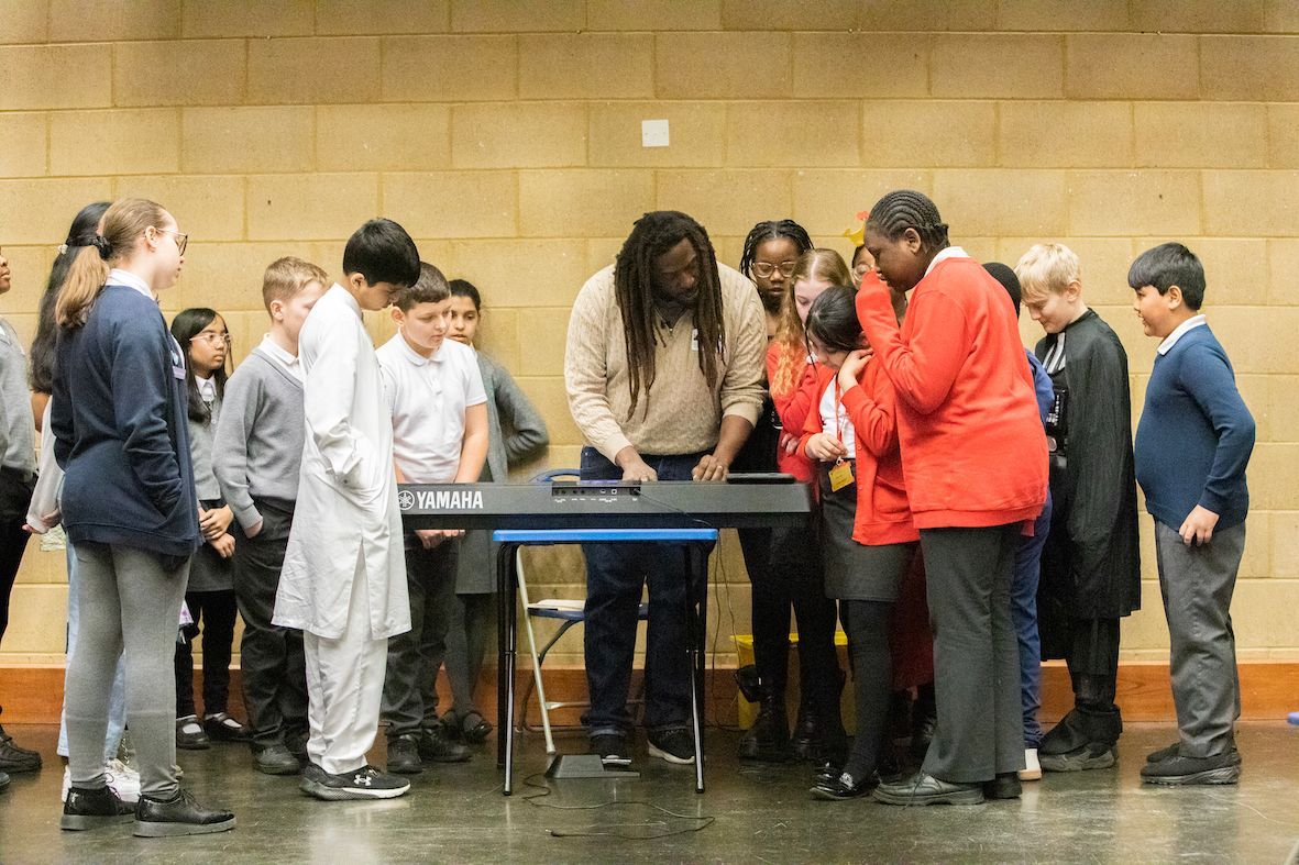 A group of children are standing around a man playing a keyboard.