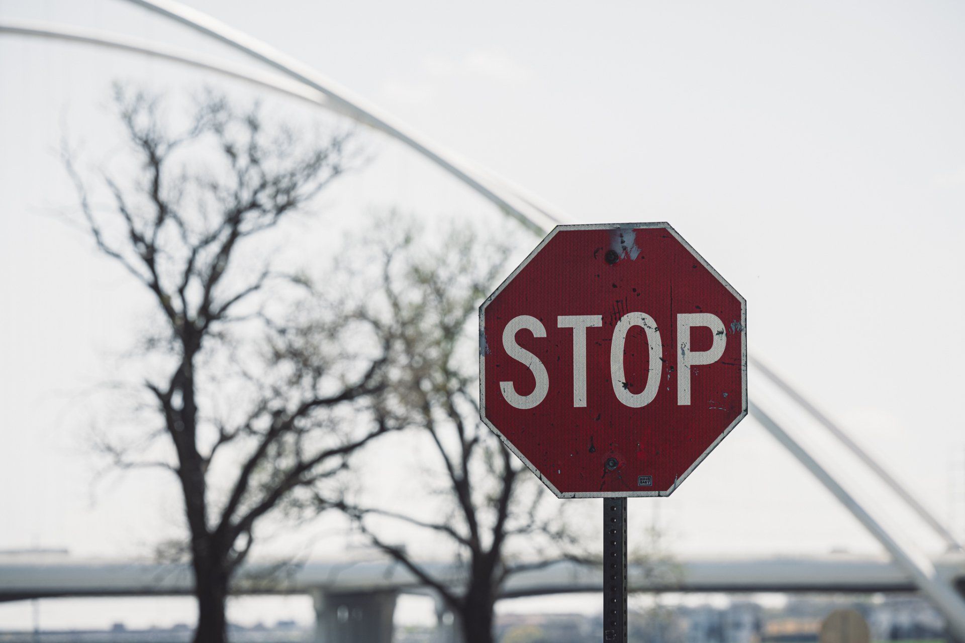 a stop sign with trees in the background and a bridge in the background